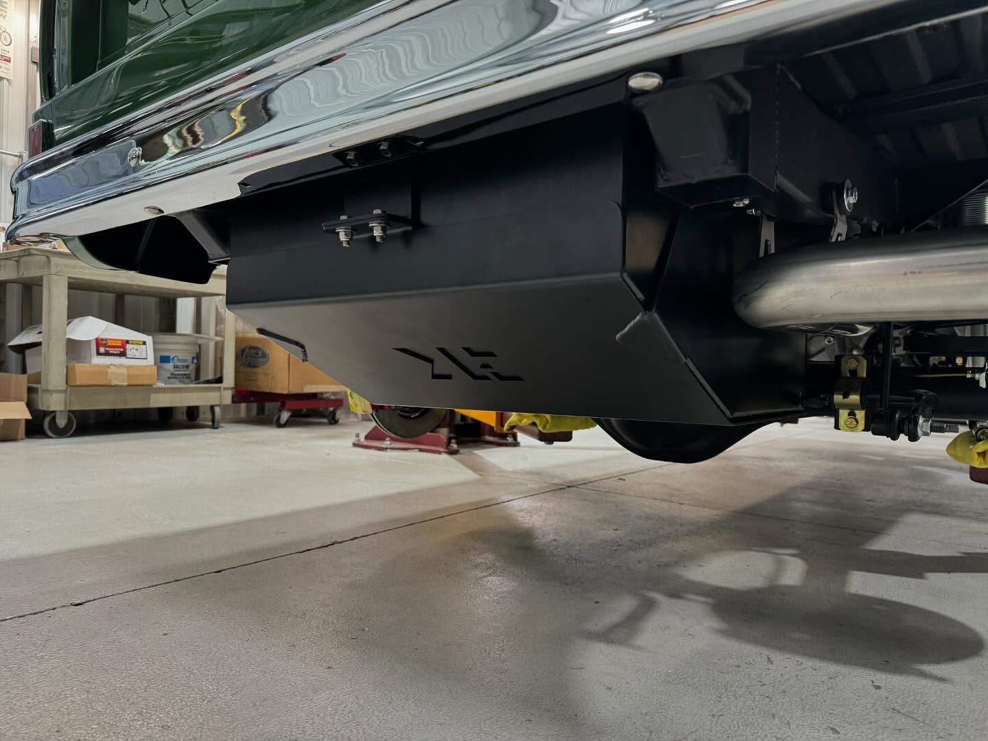 A green truck is parked in a garage with a fuel tank underneath it.