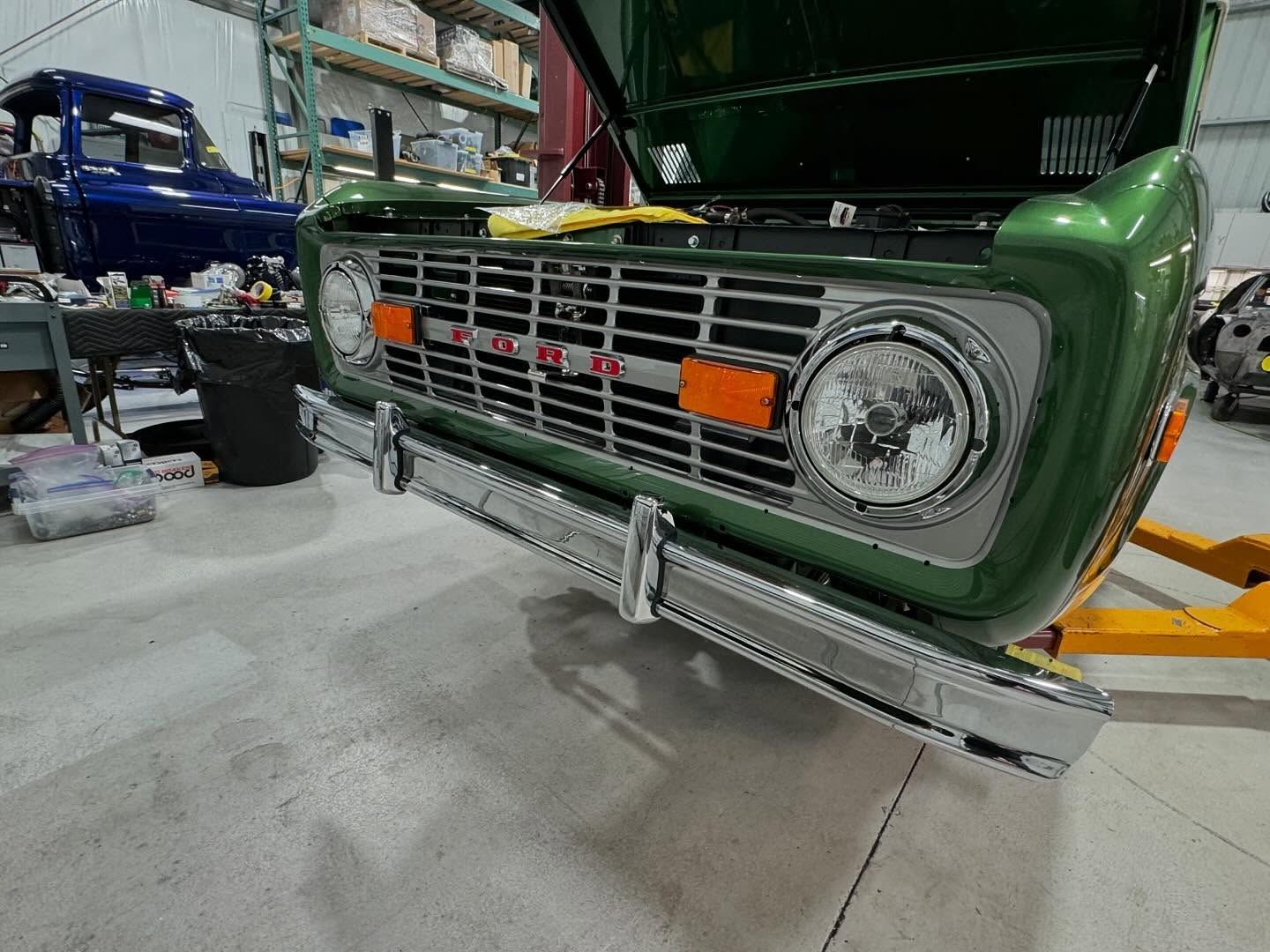 A green truck with the hood open is sitting in a garage.