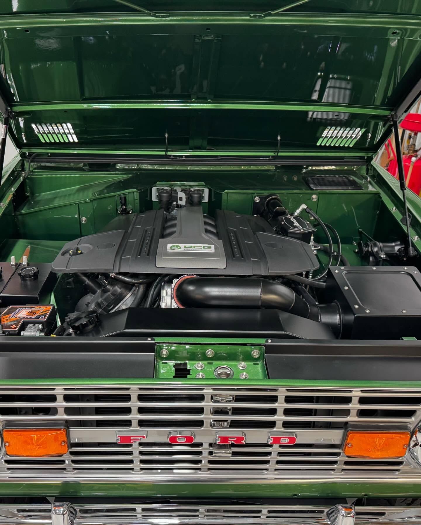 The engine of a green ford bronco with the hood open.