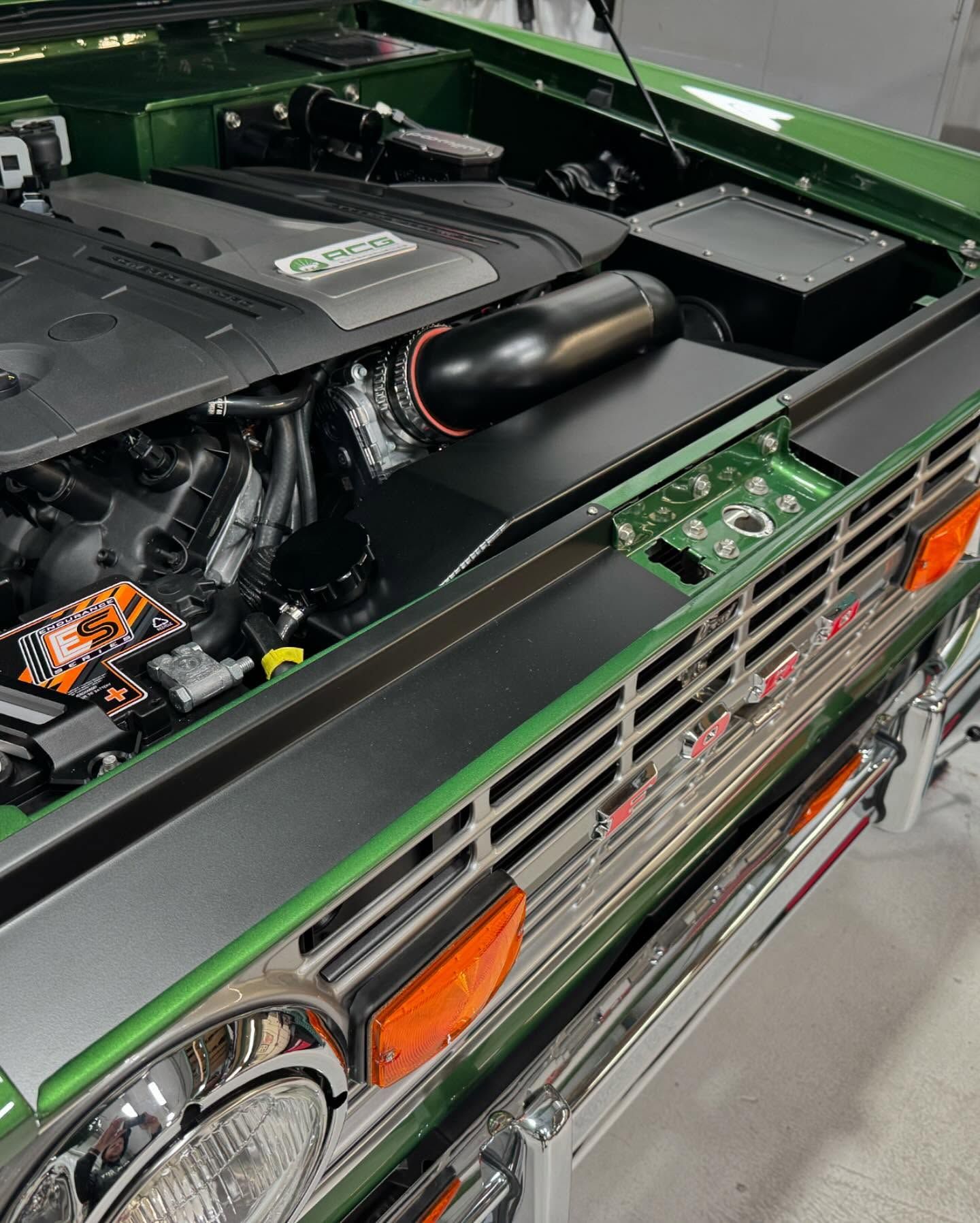 The engine of a green car is visible under the hood.