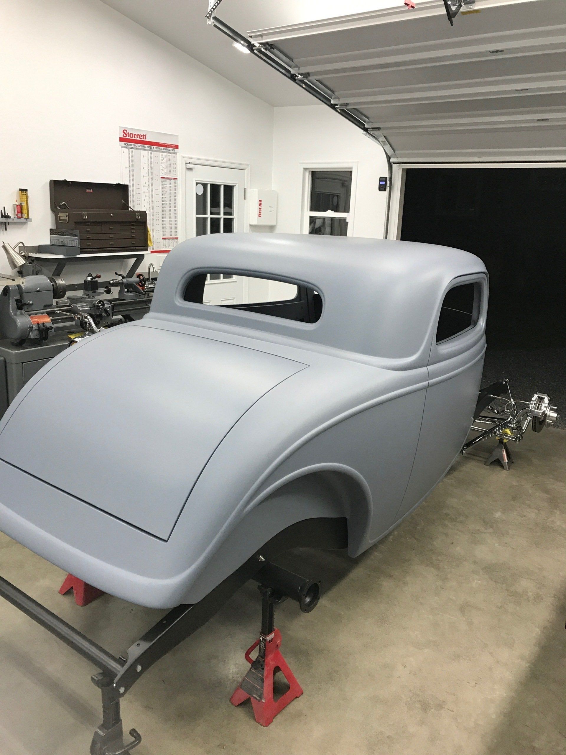 A car body is sitting on a jack stand in a garage.