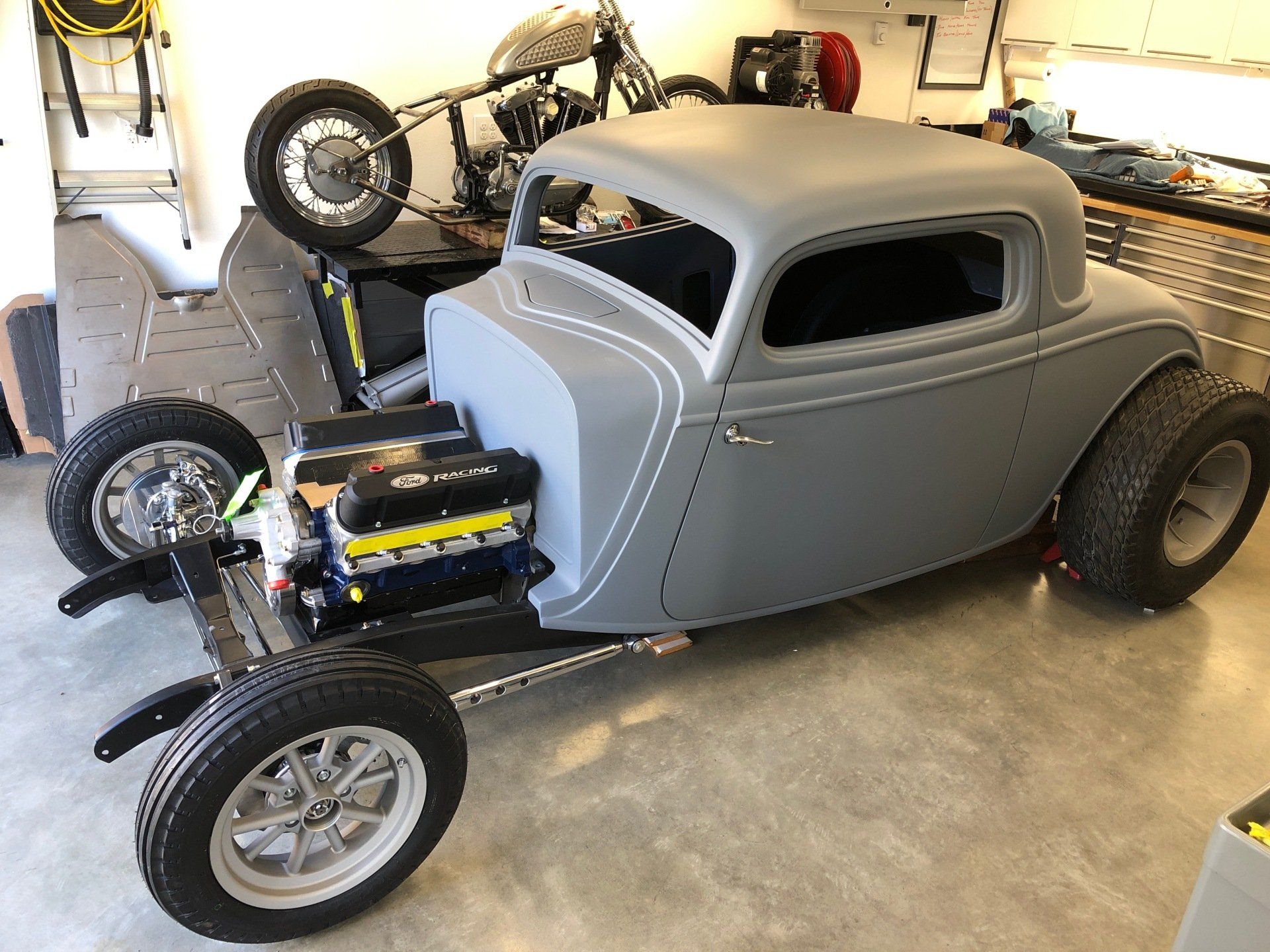 A gray hot rod is parked in a garage next to a motorcycle.