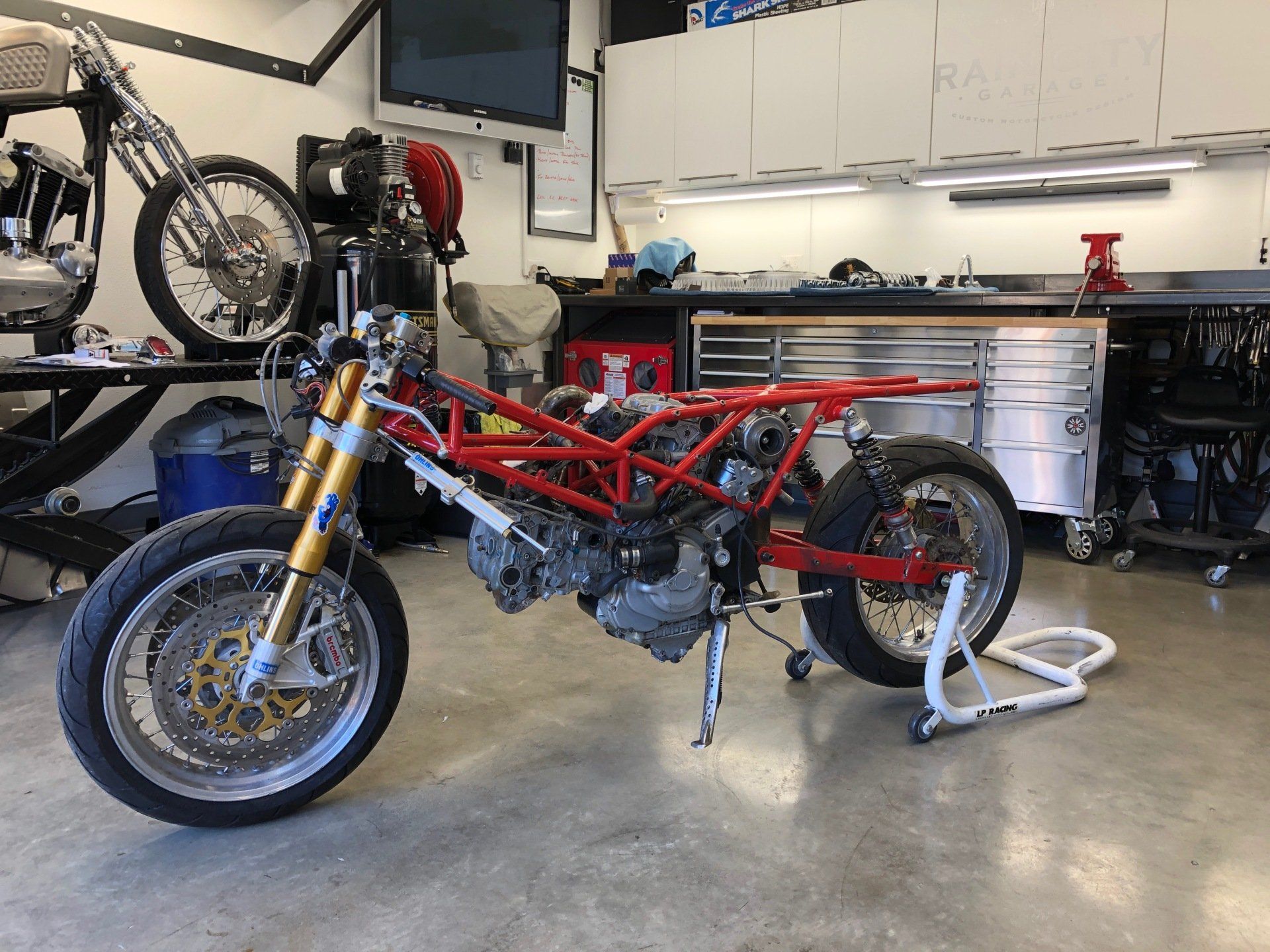A red motorcycle is sitting on a stand in a garage.