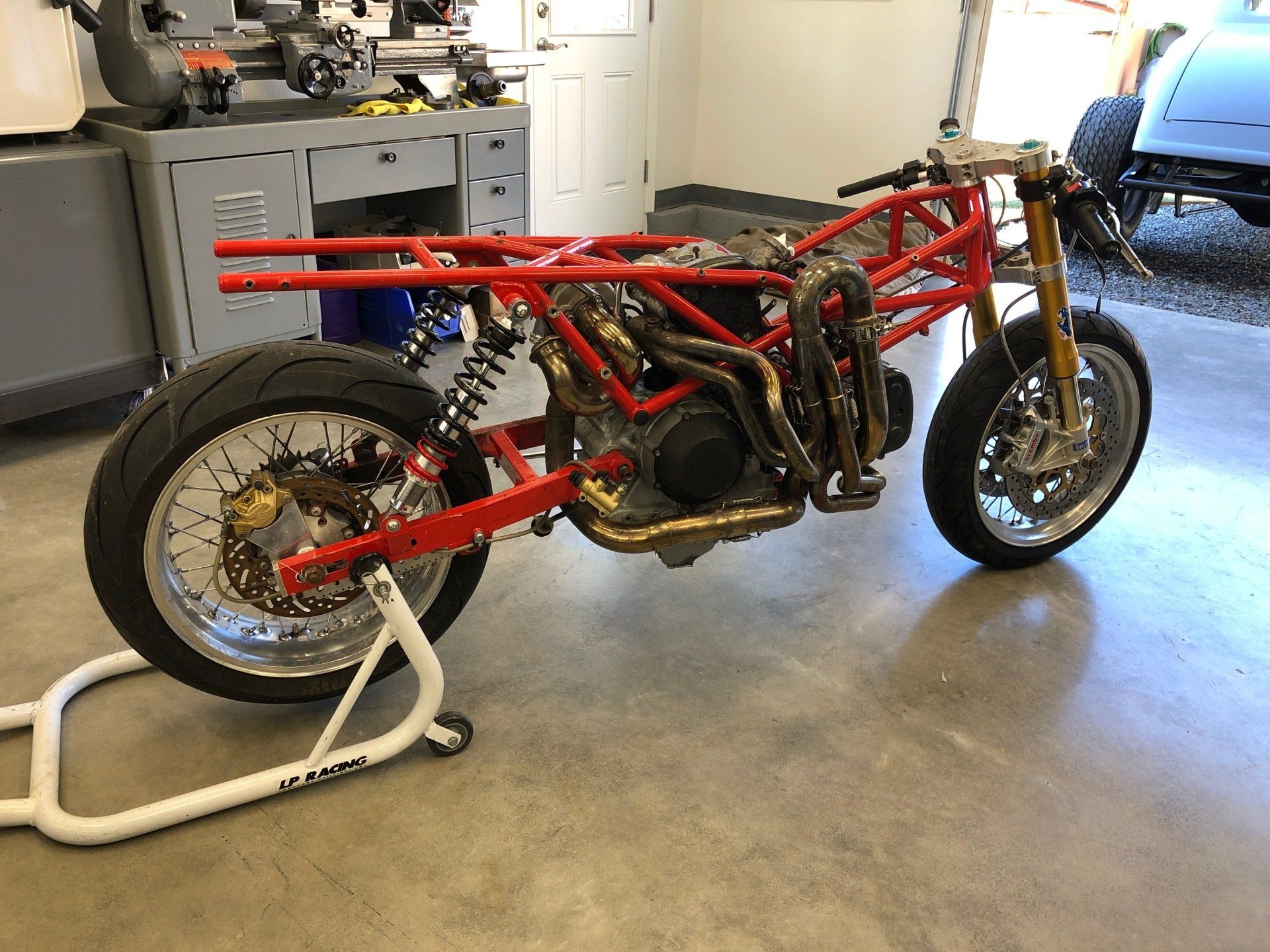 A red motorcycle is sitting on a stand in a garage.