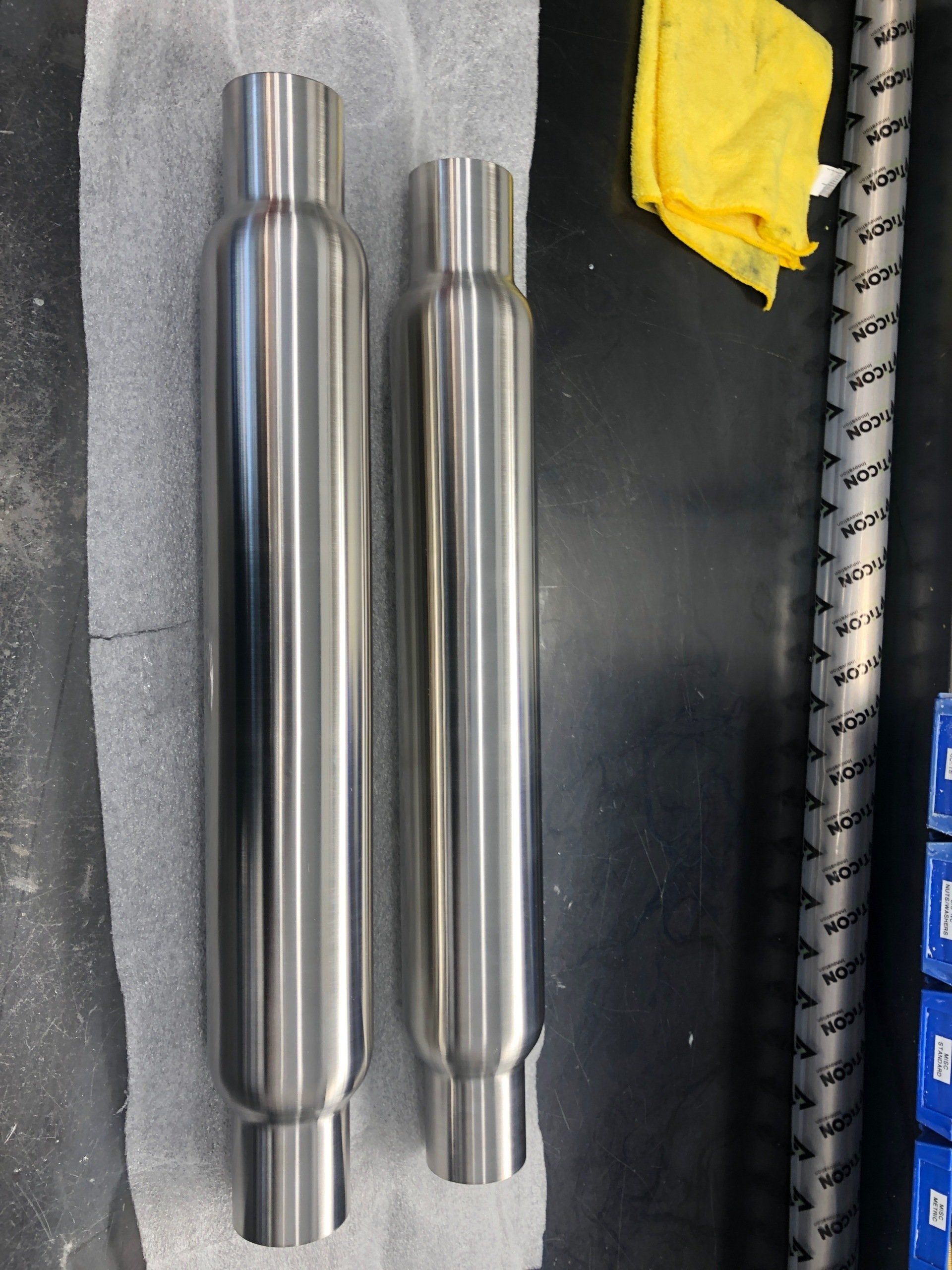 Two stainless steel pipes are sitting on a table next to a yellow cloth
