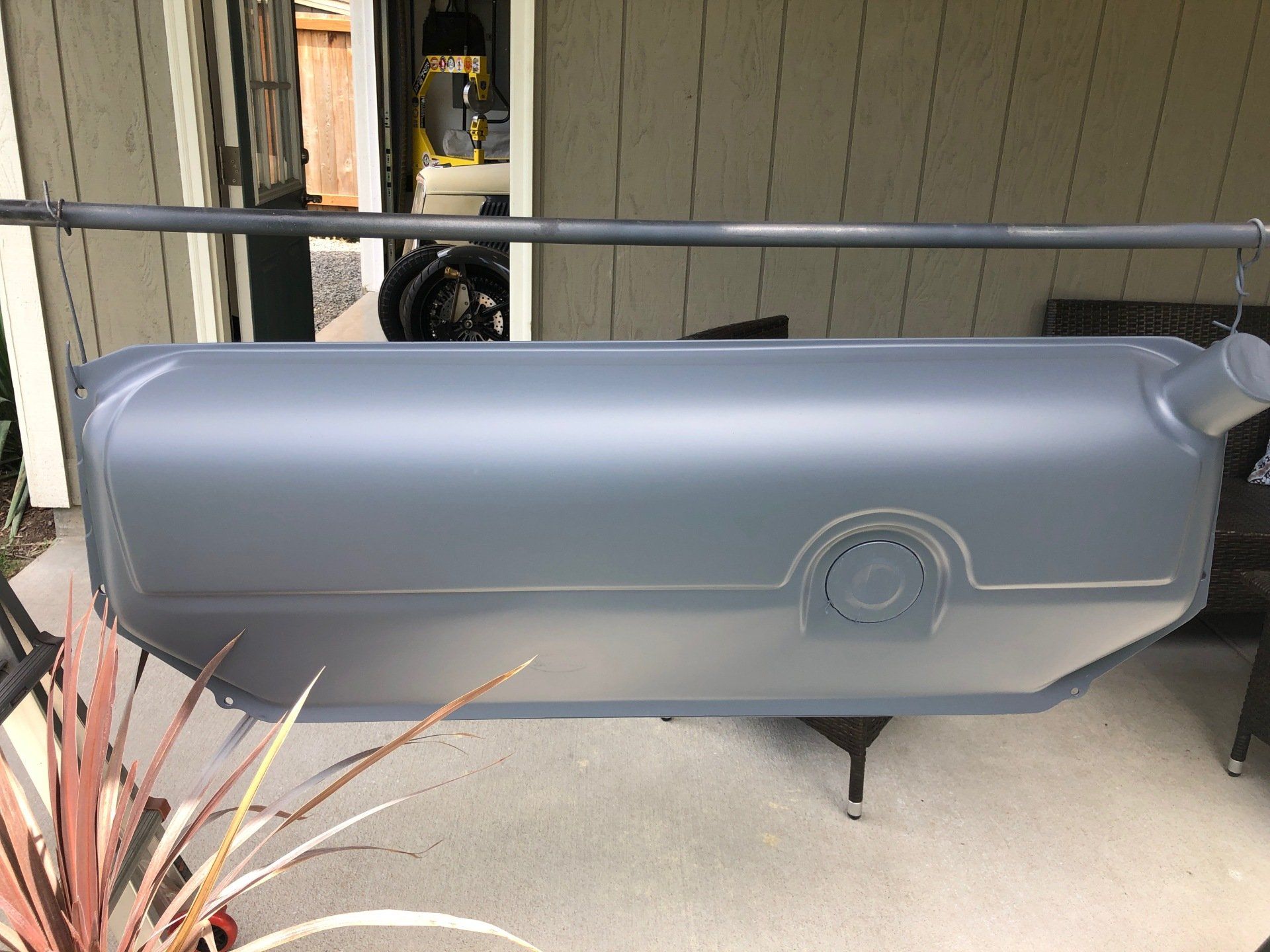 A gray fuel tank is sitting on a porch next to a plant.