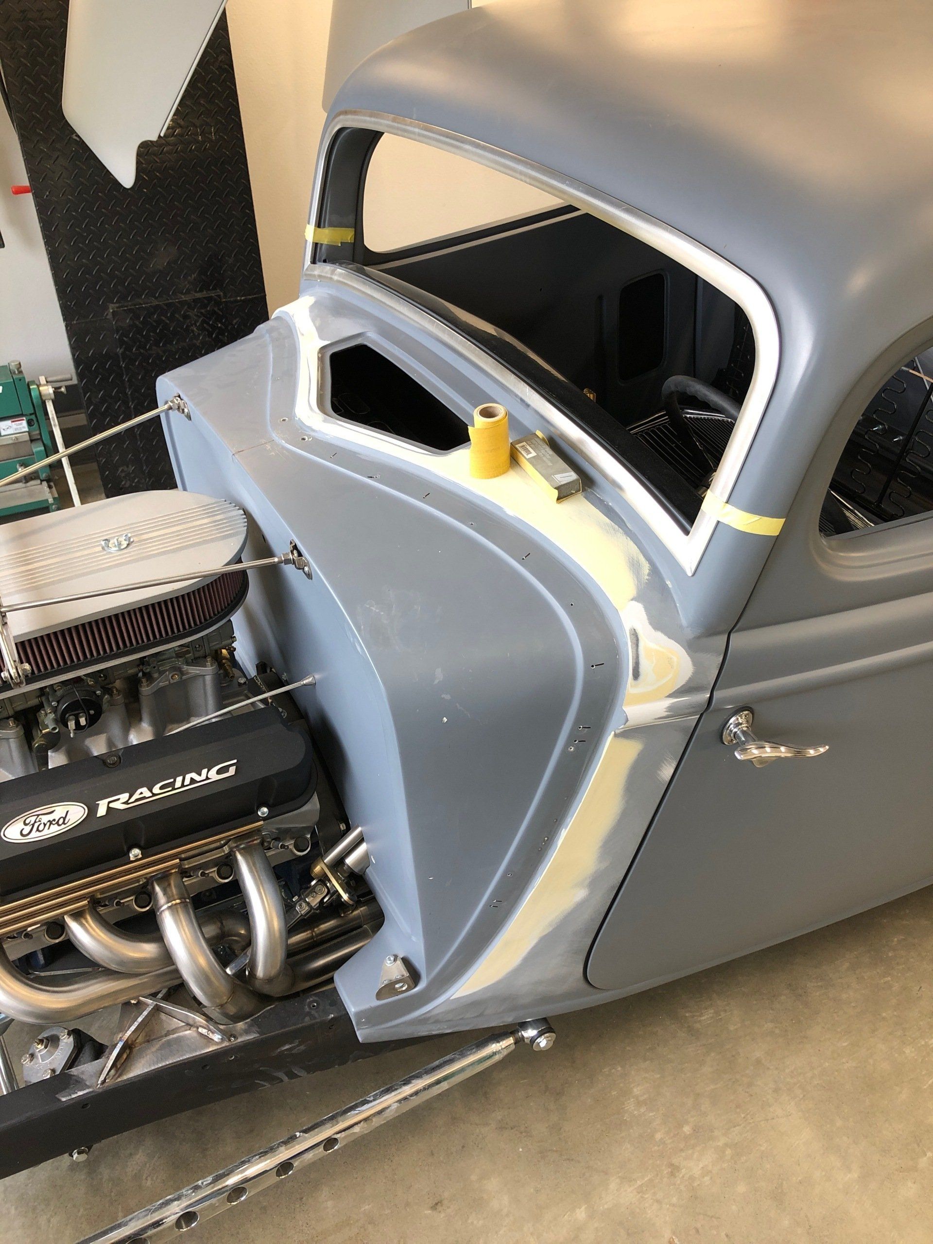 A gray car with a large engine is sitting in a garage.