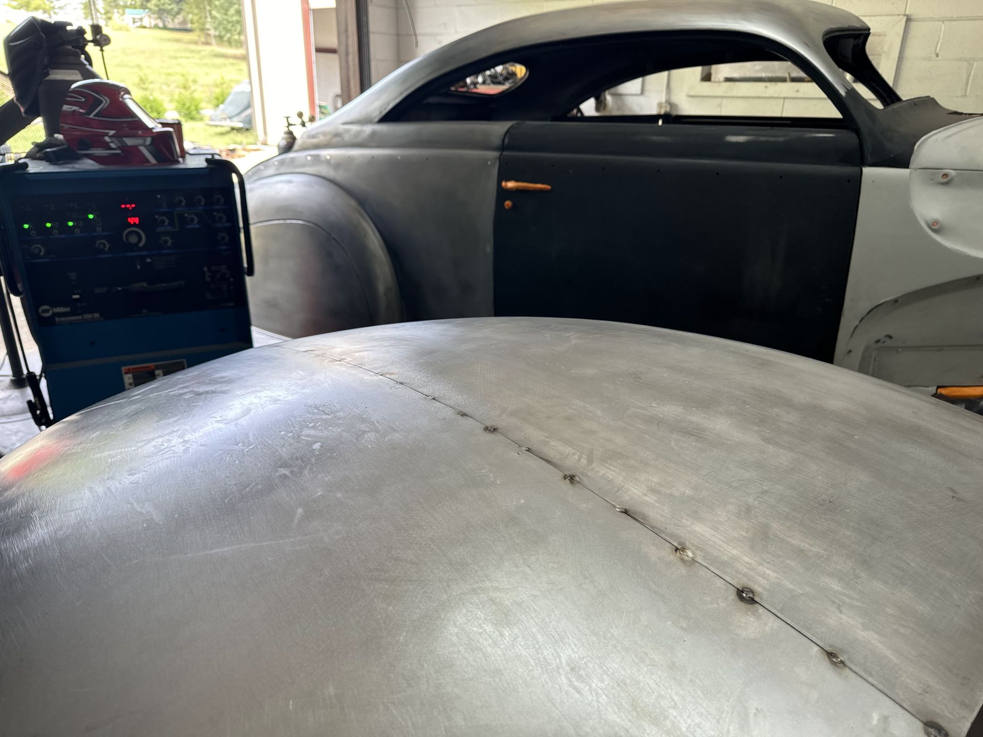 A silver car is sitting in a garage next to a welding machine
