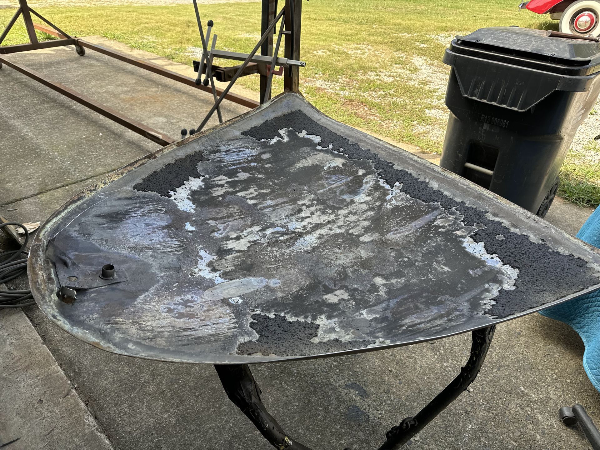 A piece of metal is sitting on a sidewalk next to a trash can.