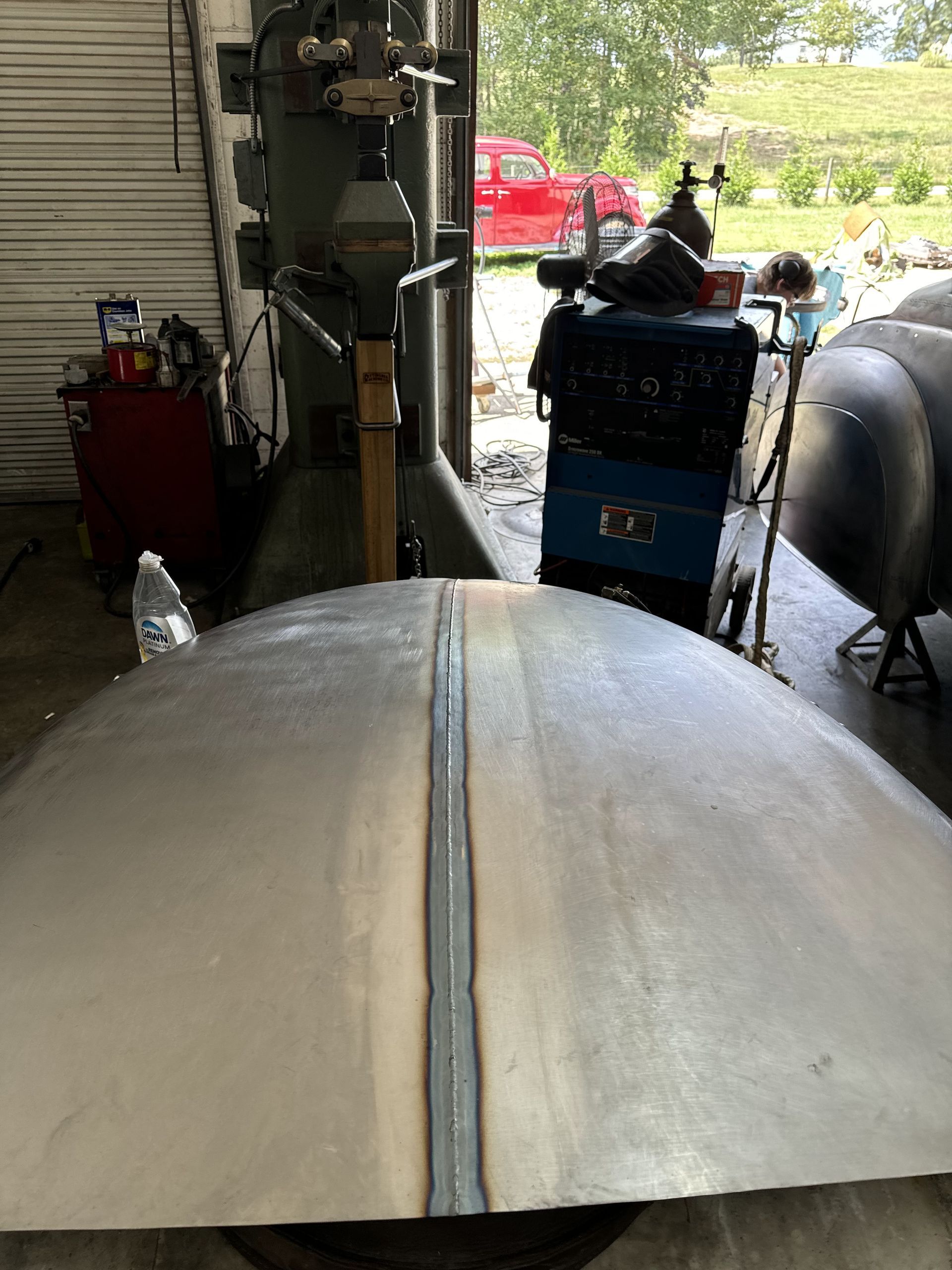 A large piece of metal is sitting in a garage next to a welding machine.