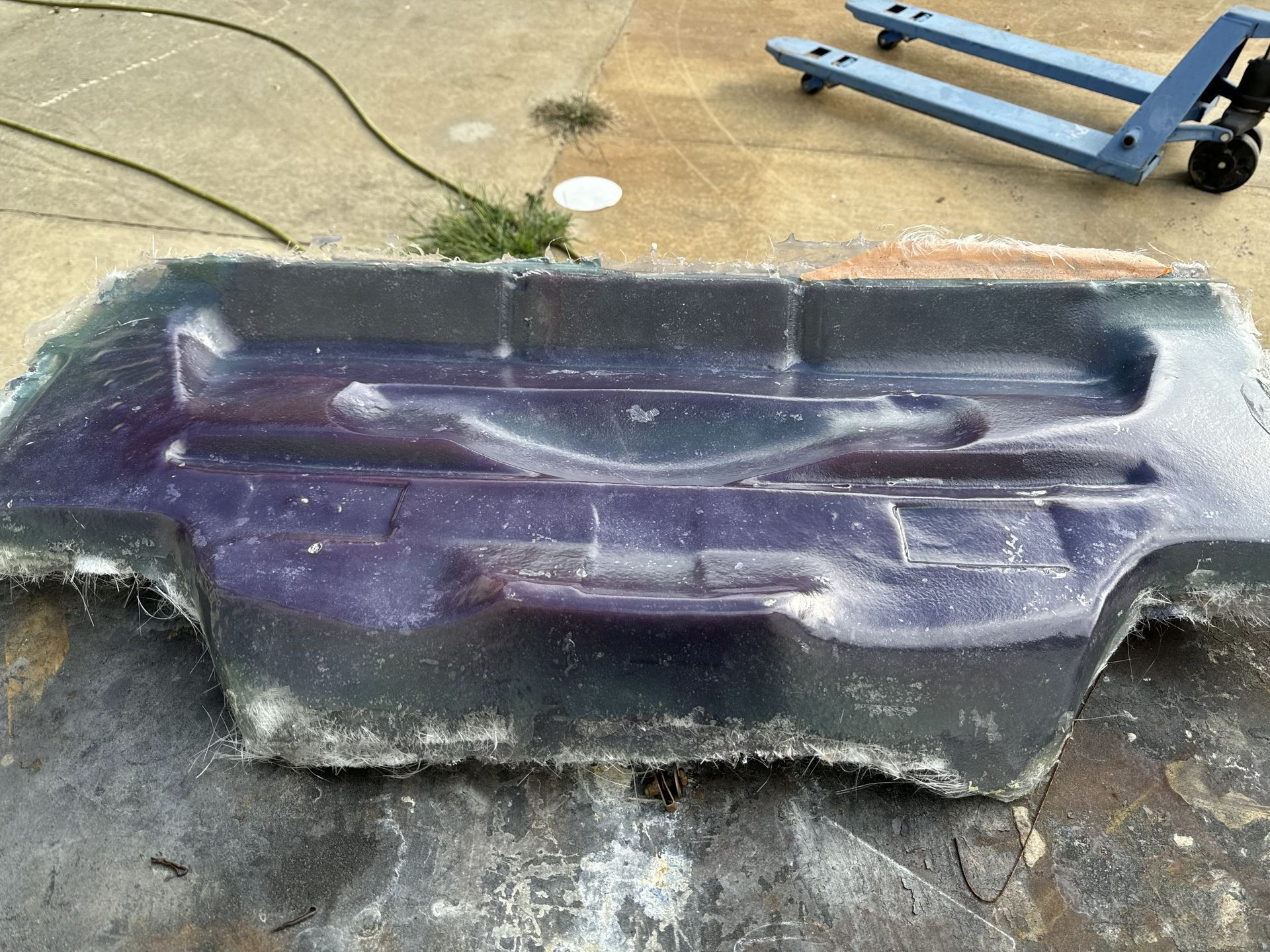 A purple object is sitting on the ground next to a blue forklift.