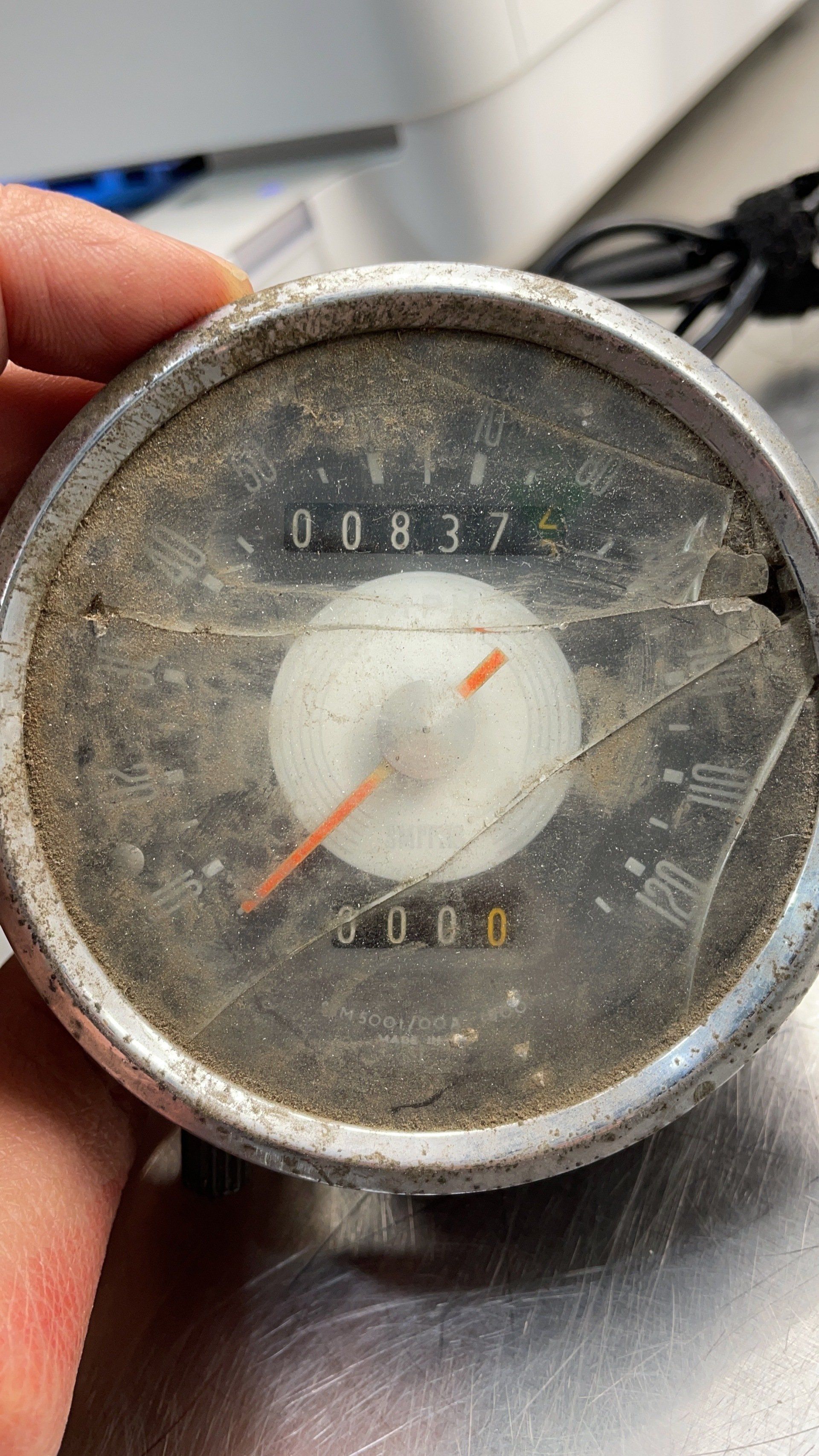 A person is holding an old speedometer with a broken glass cover.