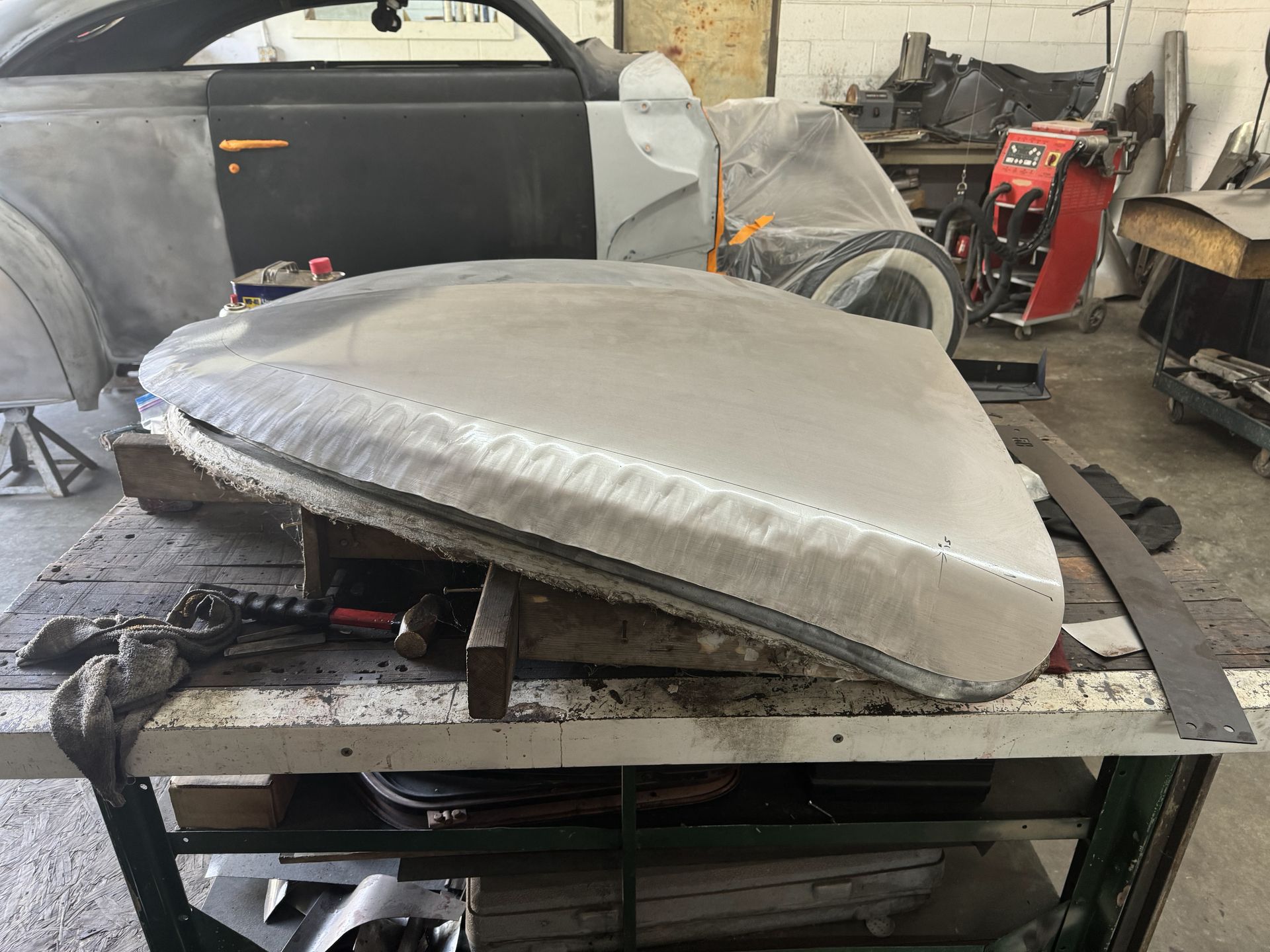 A large piece of metal is sitting on a table in a garage next to a car.