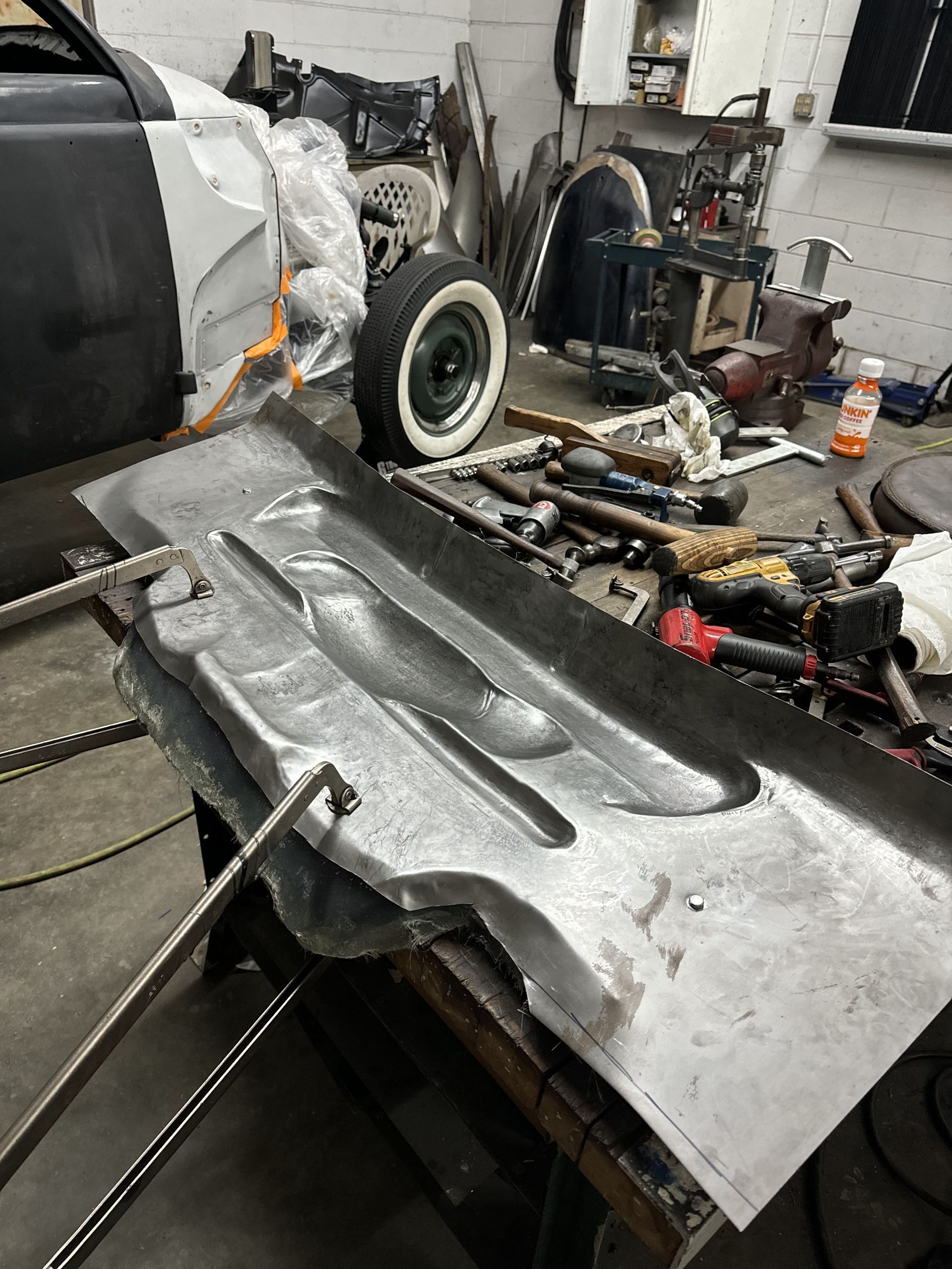A piece of metal is sitting on top of a table in a garage next to a car.