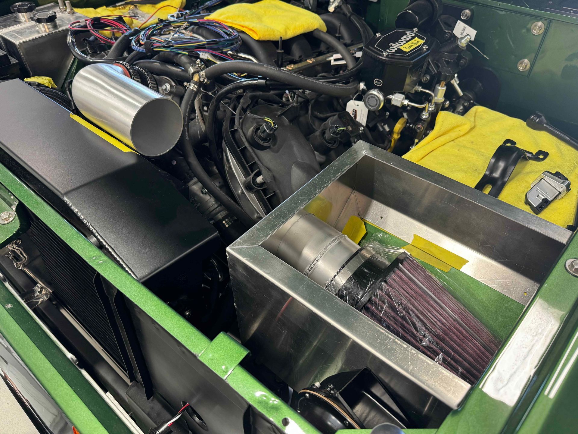 A green car with a stainless steel air filter in the engine compartment.
