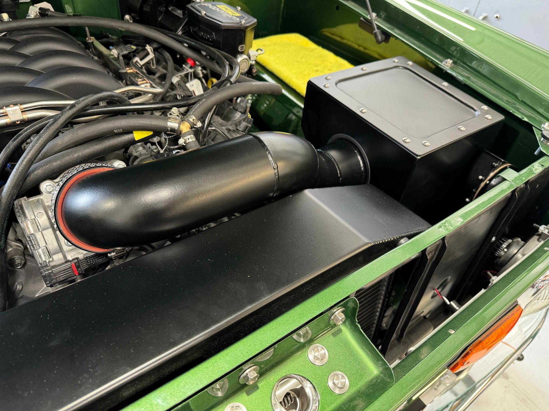 A green car with the hood open and a black pipe coming out of the engine.