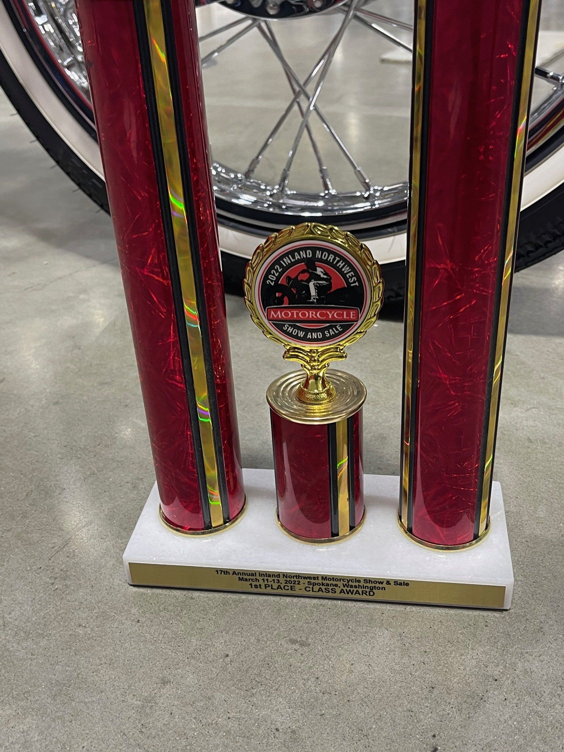 A red and gold trophy is sitting next to a motorcycle wheel.