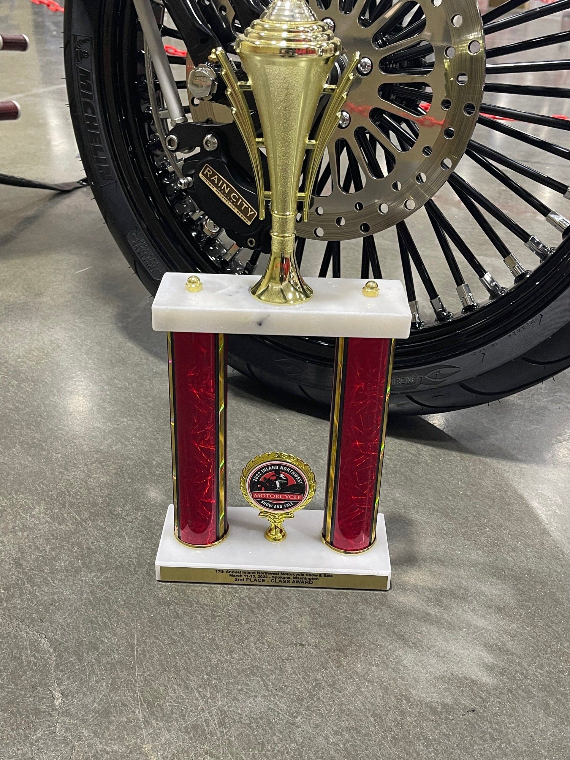 A trophy is sitting in front of a motorcycle wheel.