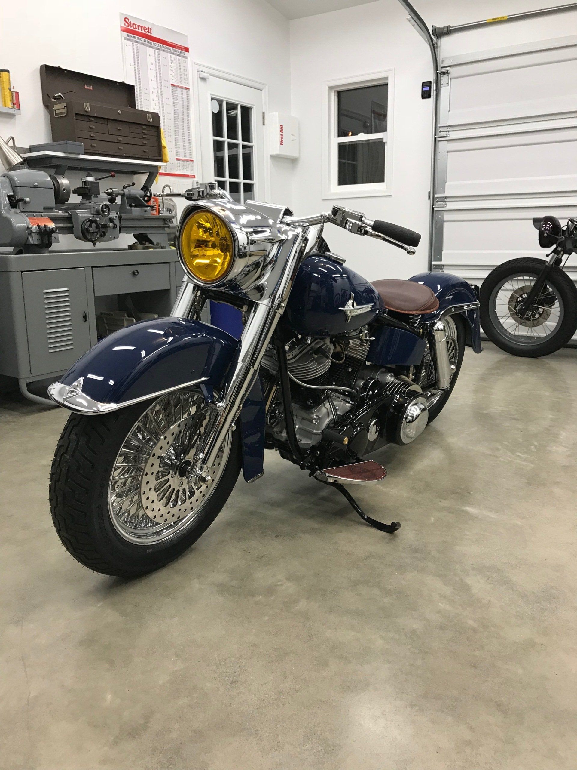 A blue motorcycle is parked in a garage next to another motorcycle.