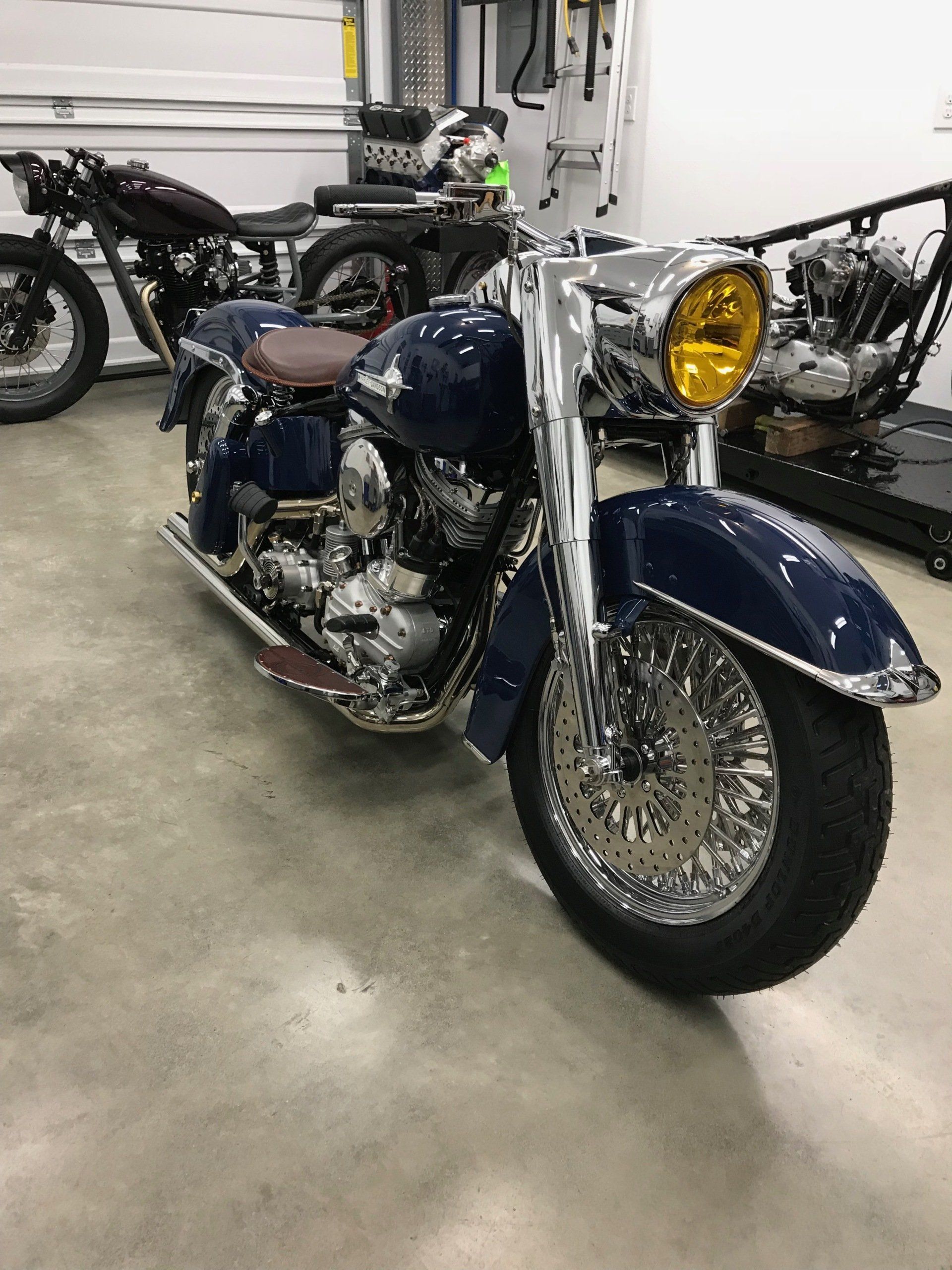 A blue motorcycle is parked in a garage next to other motorcycles.