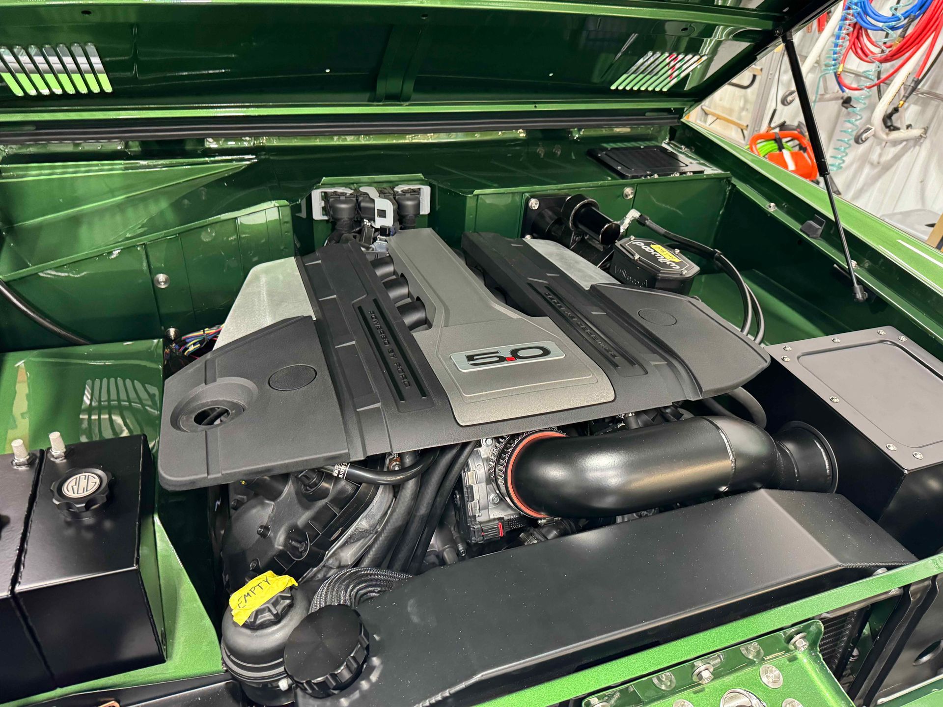 The engine of a green car is shown with the hood open.