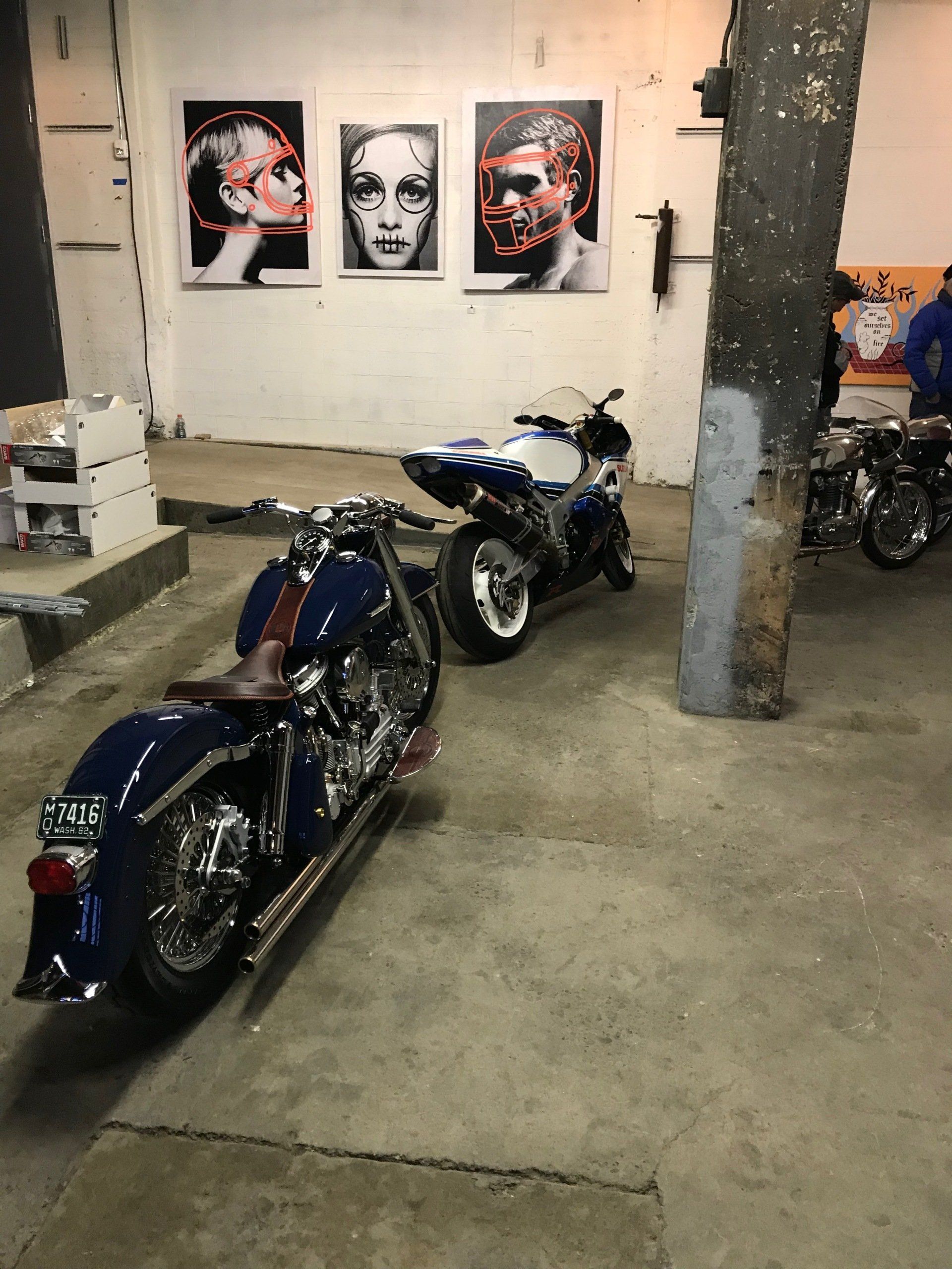 Two motorcycles are parked in a garage with paintings on the wall