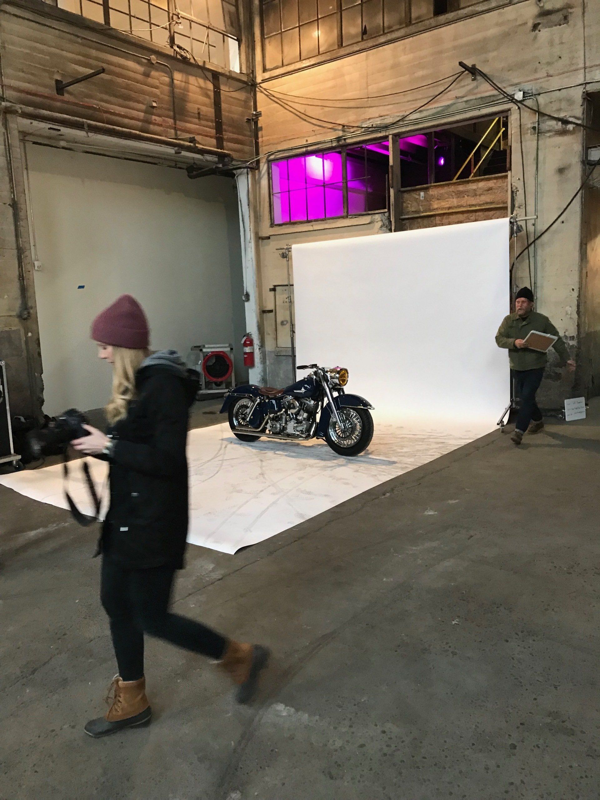 A woman is taking a picture of a motorcycle in a warehouse.