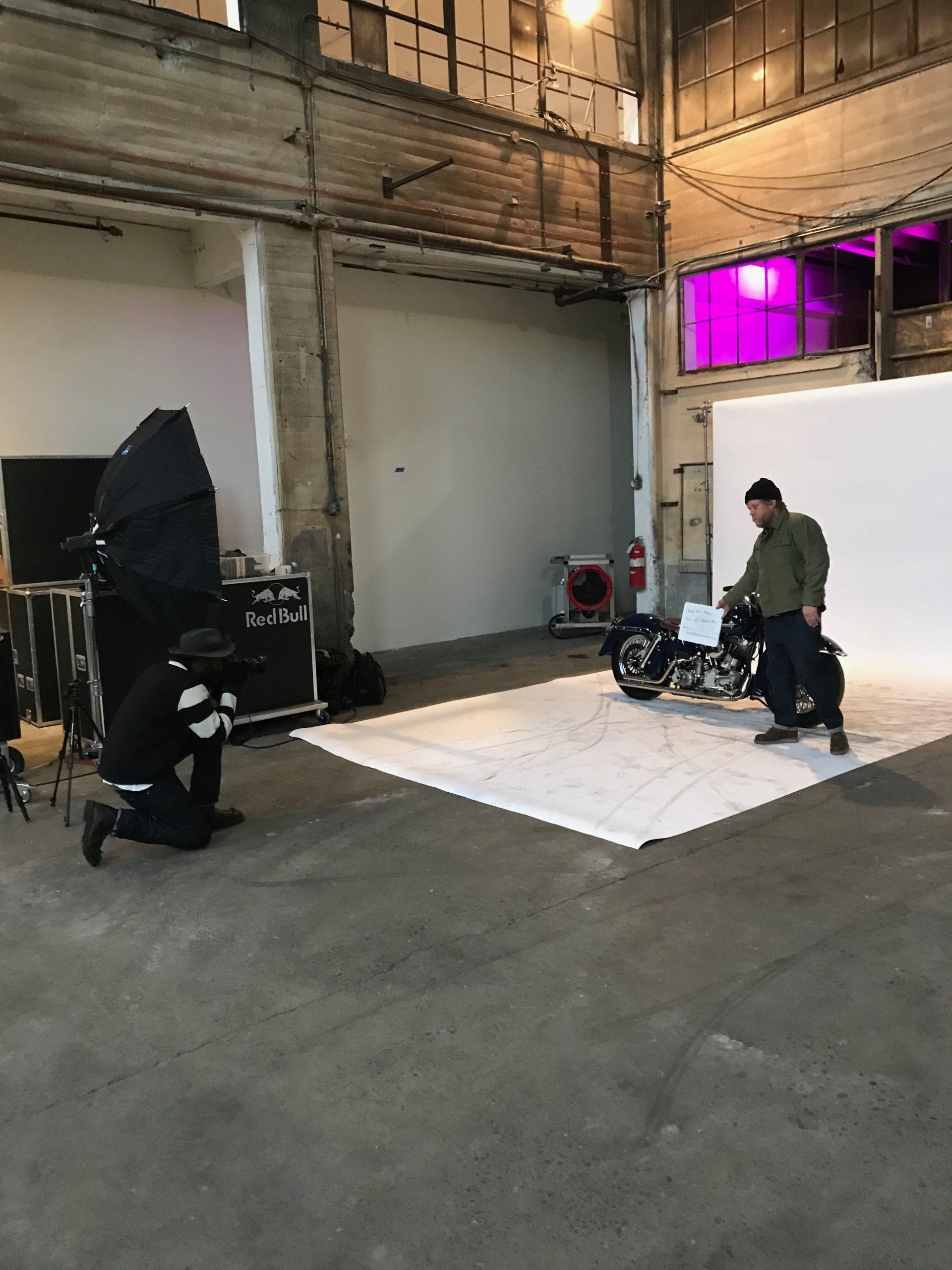 A man is kneeling down in front of a motorcycle in a photo studio.