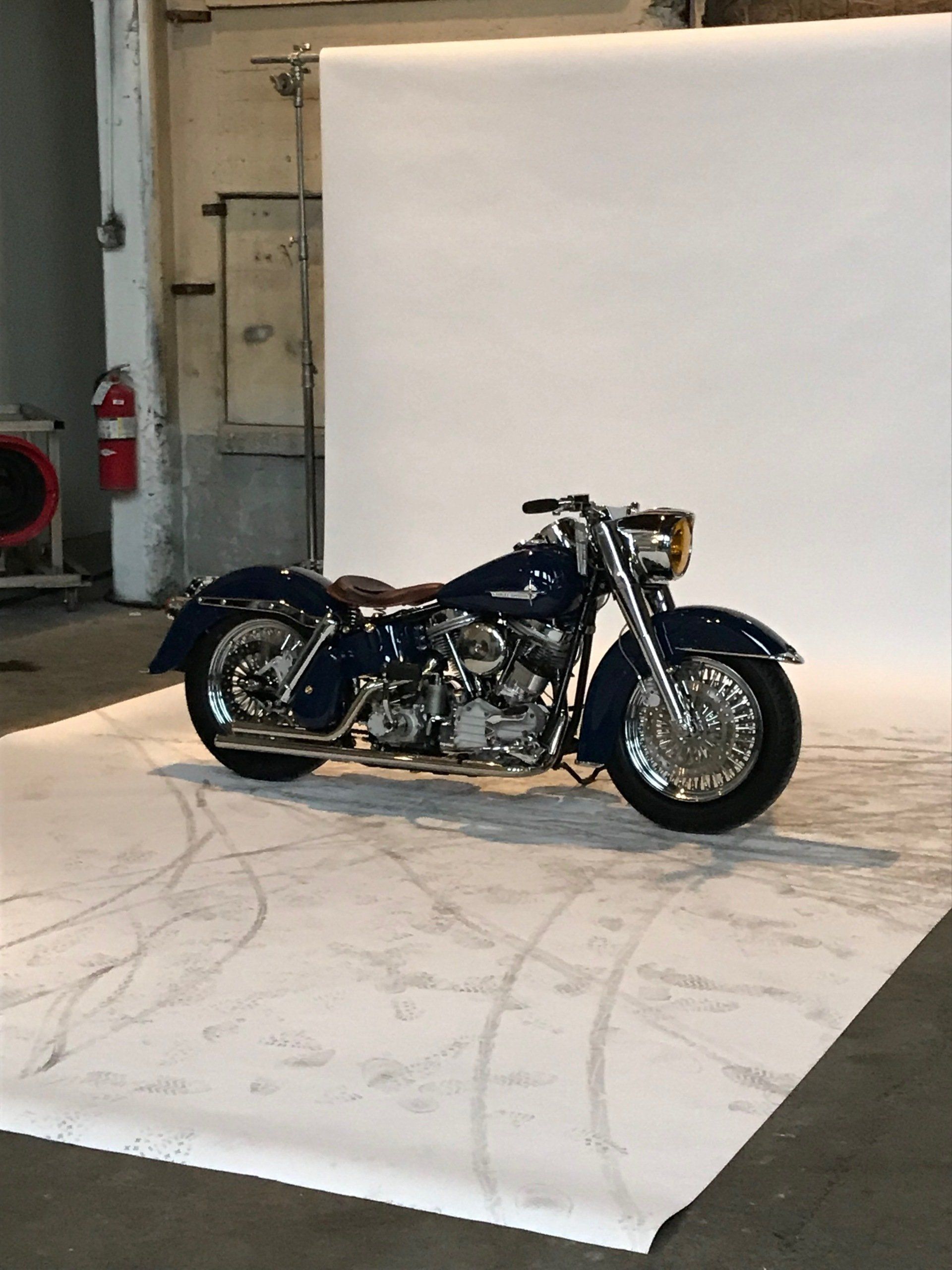 A blue motorcycle is parked in front of a white wall.