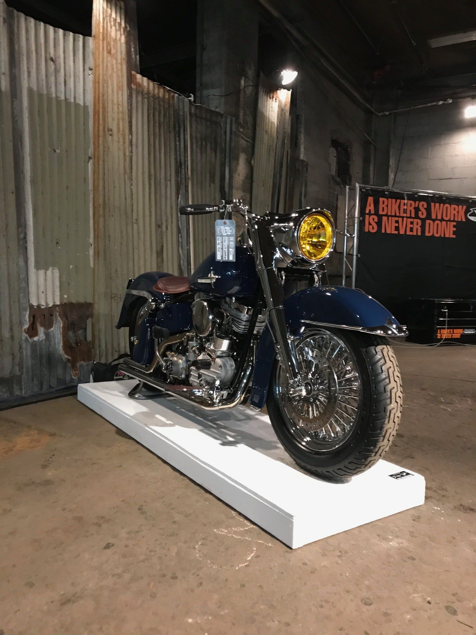 A blue motorcycle is parked on a white display in a garage.