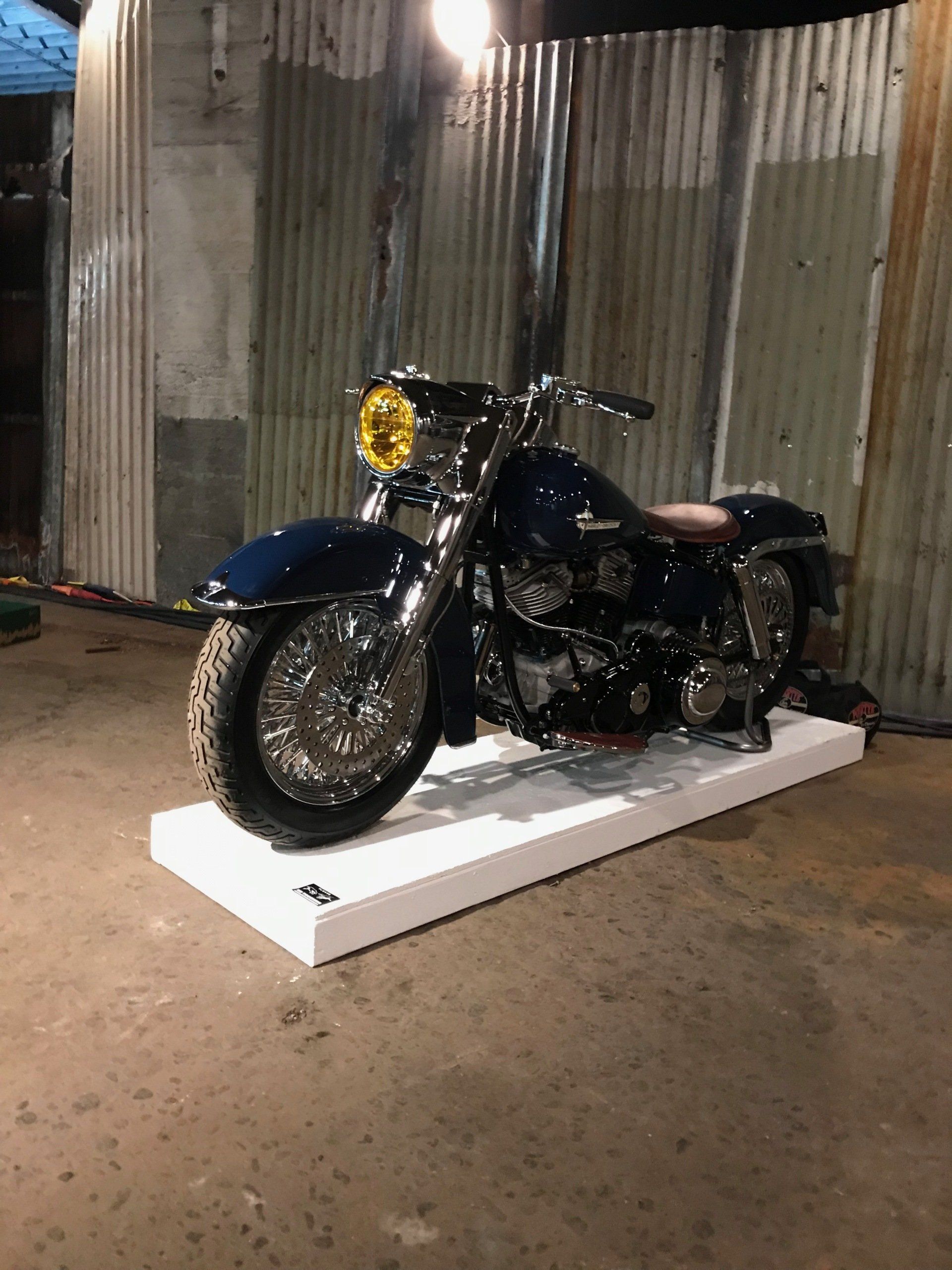 A blue motorcycle is parked on a white display in a garage.