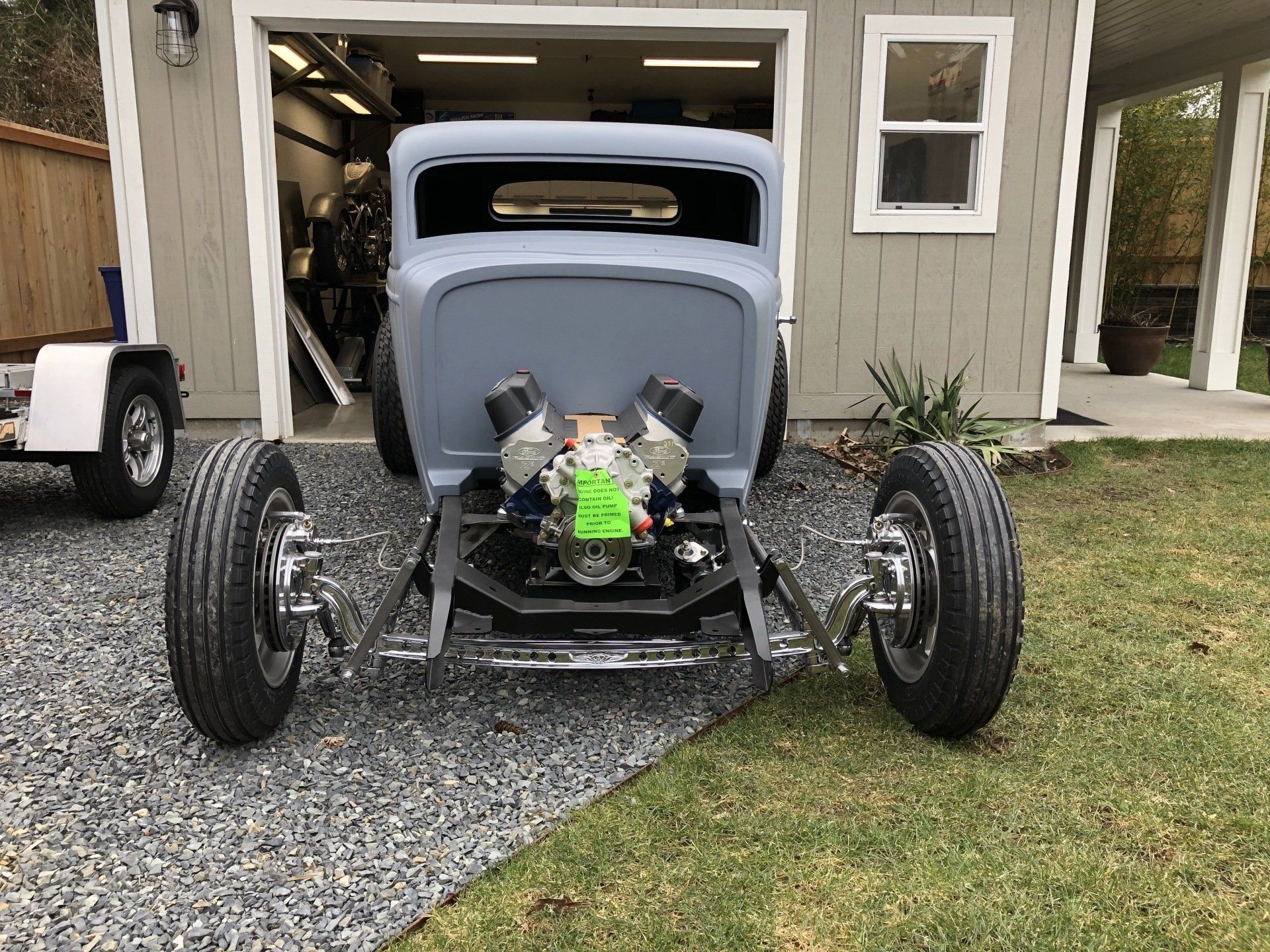 A hot rod is parked in front of a garage with the door open.