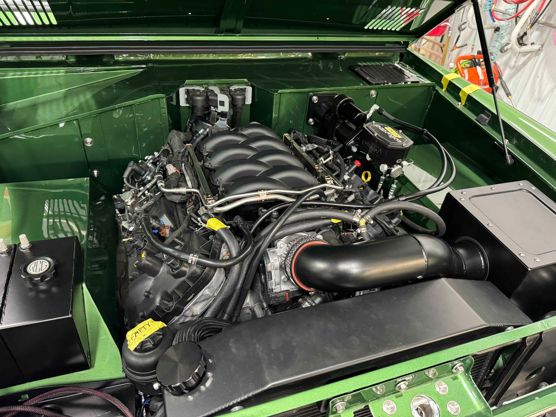 A green car with a black engine is sitting in a garage.