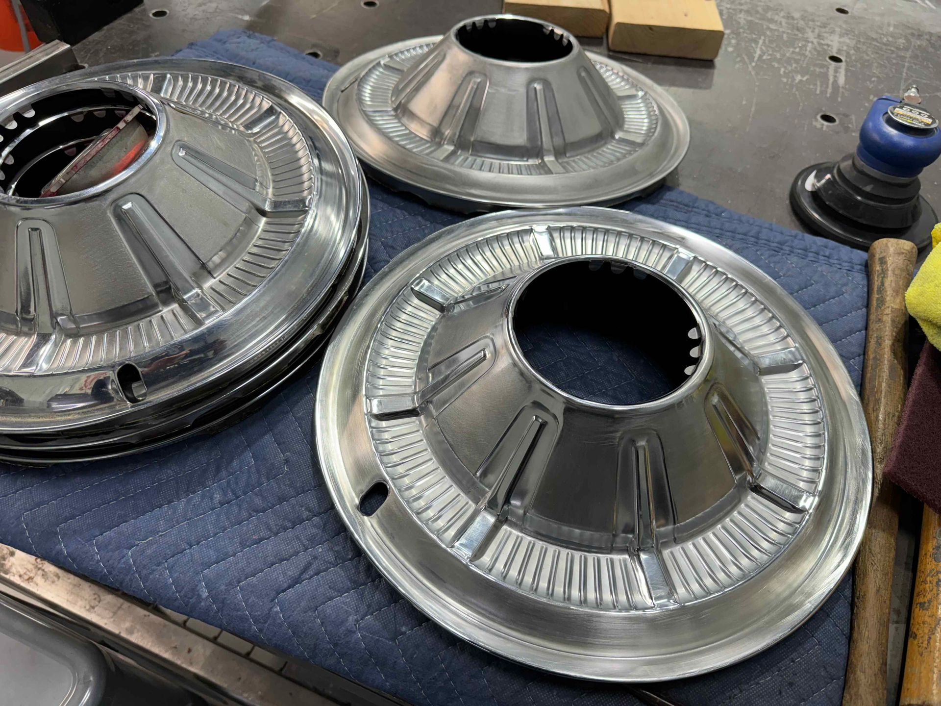 Three chrome wheel covers are sitting on top of a blue blanket on a table.