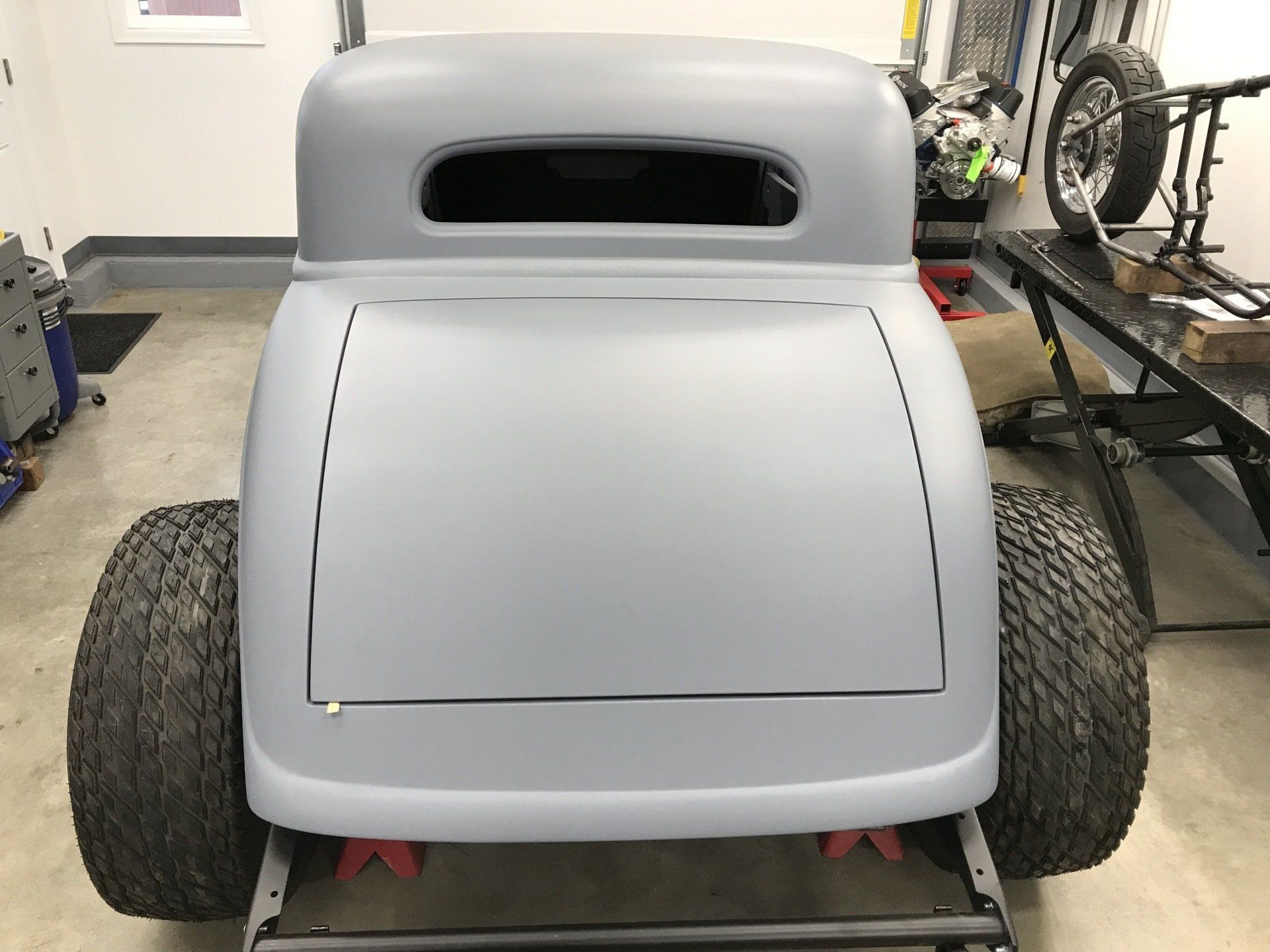 A grey car is sitting on a trailer in a garage.