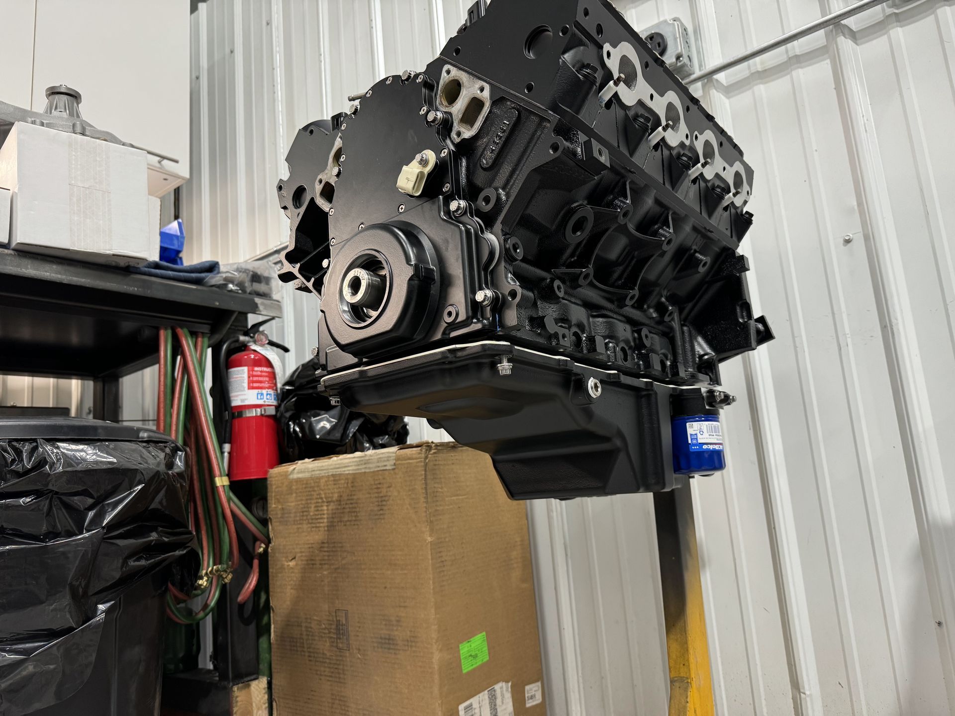 A black engine is sitting on top of a cardboard box in a garage.