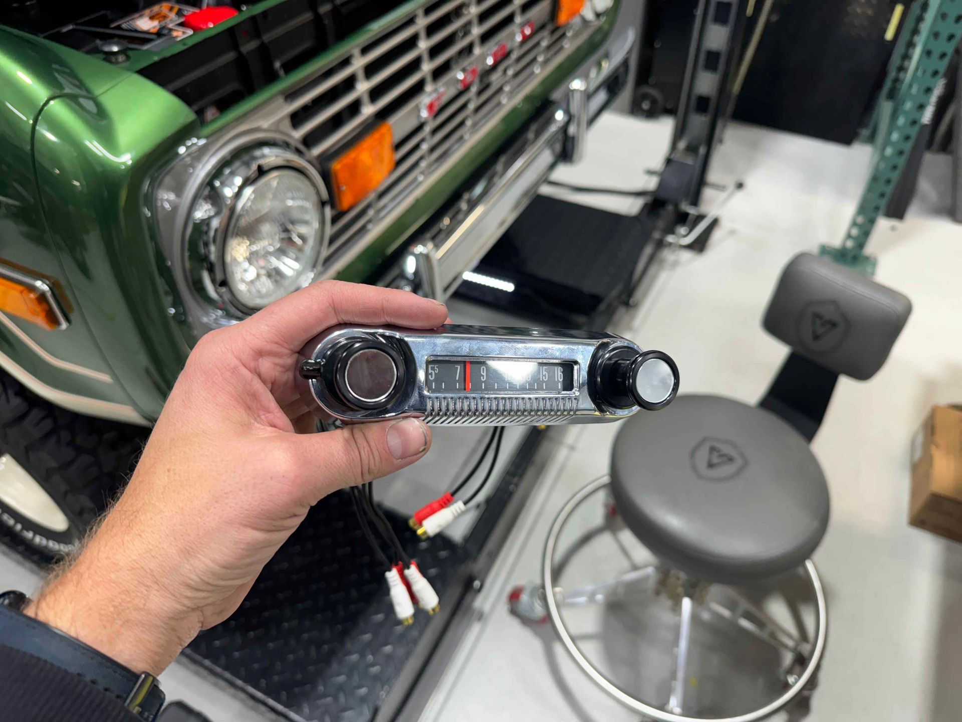 A person is holding a radio in front of a green car.