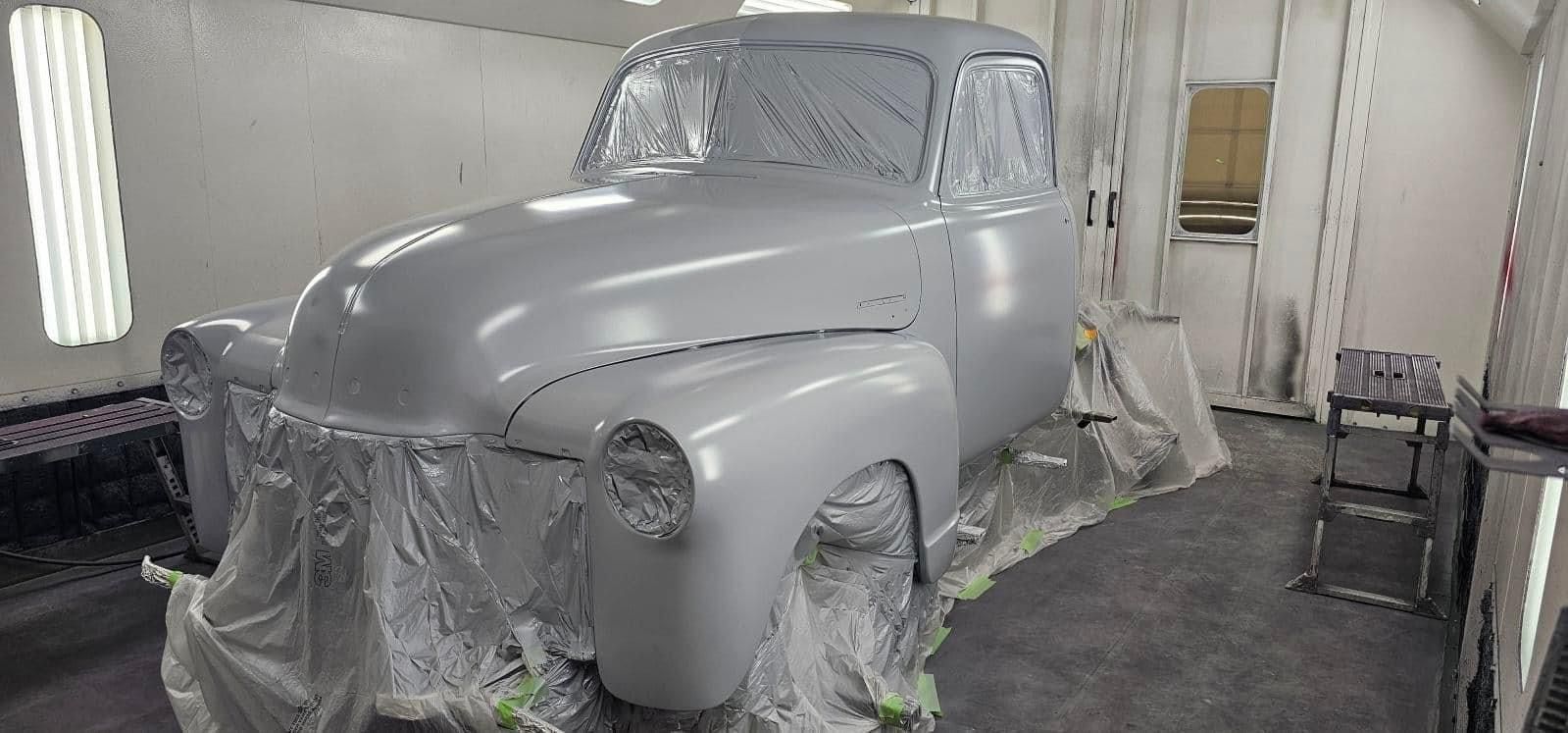 An old car is being painted in a paint booth.