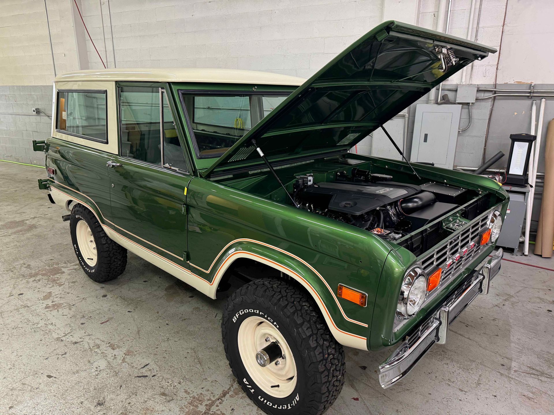 A green and white ford bronco with the hood up in a garage.