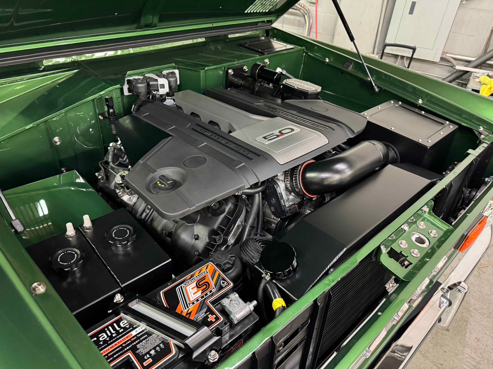 The engine of a green car is shown with the hood open.