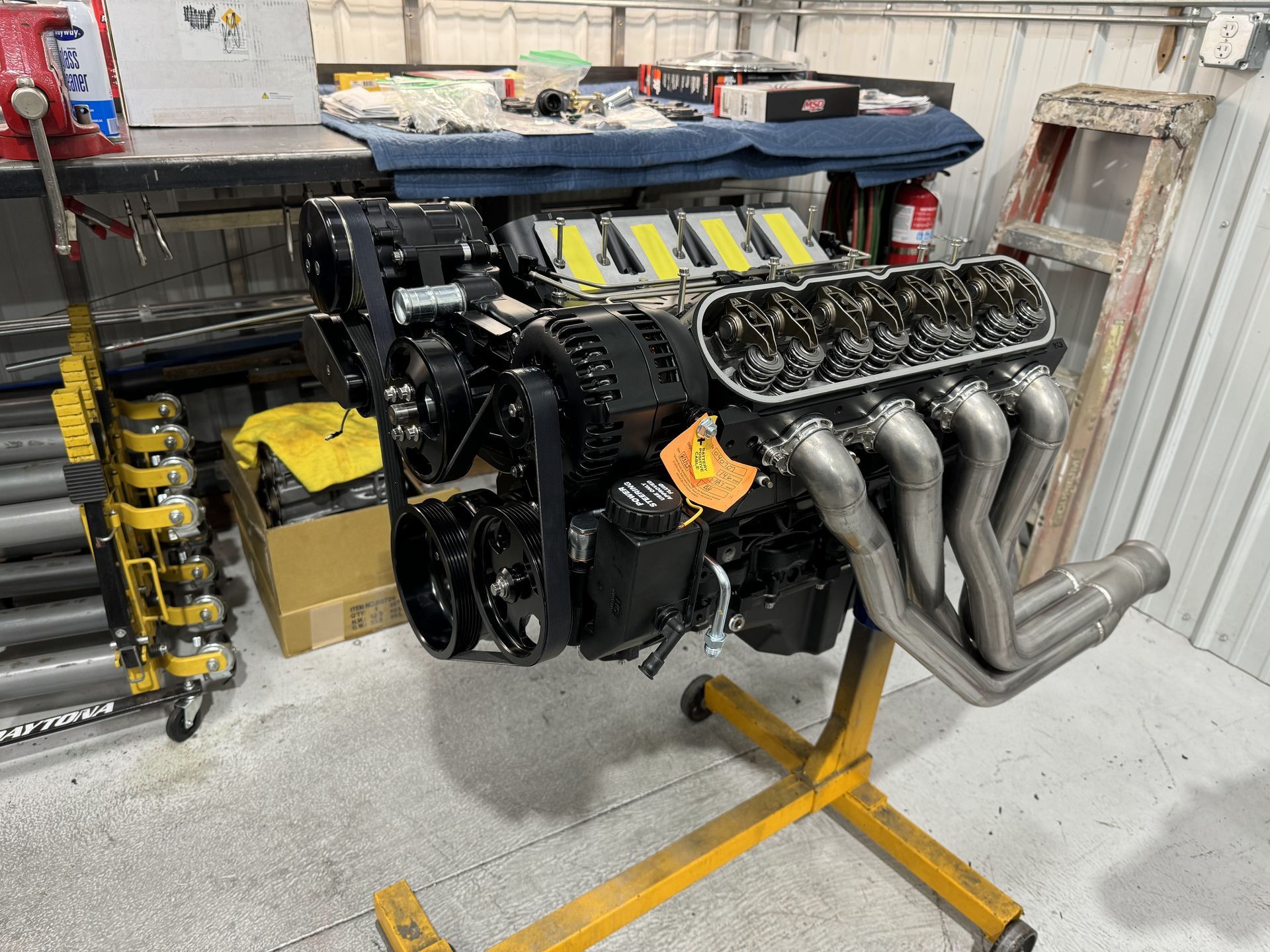 A large engine is sitting on top of a yellow stand in a garage.