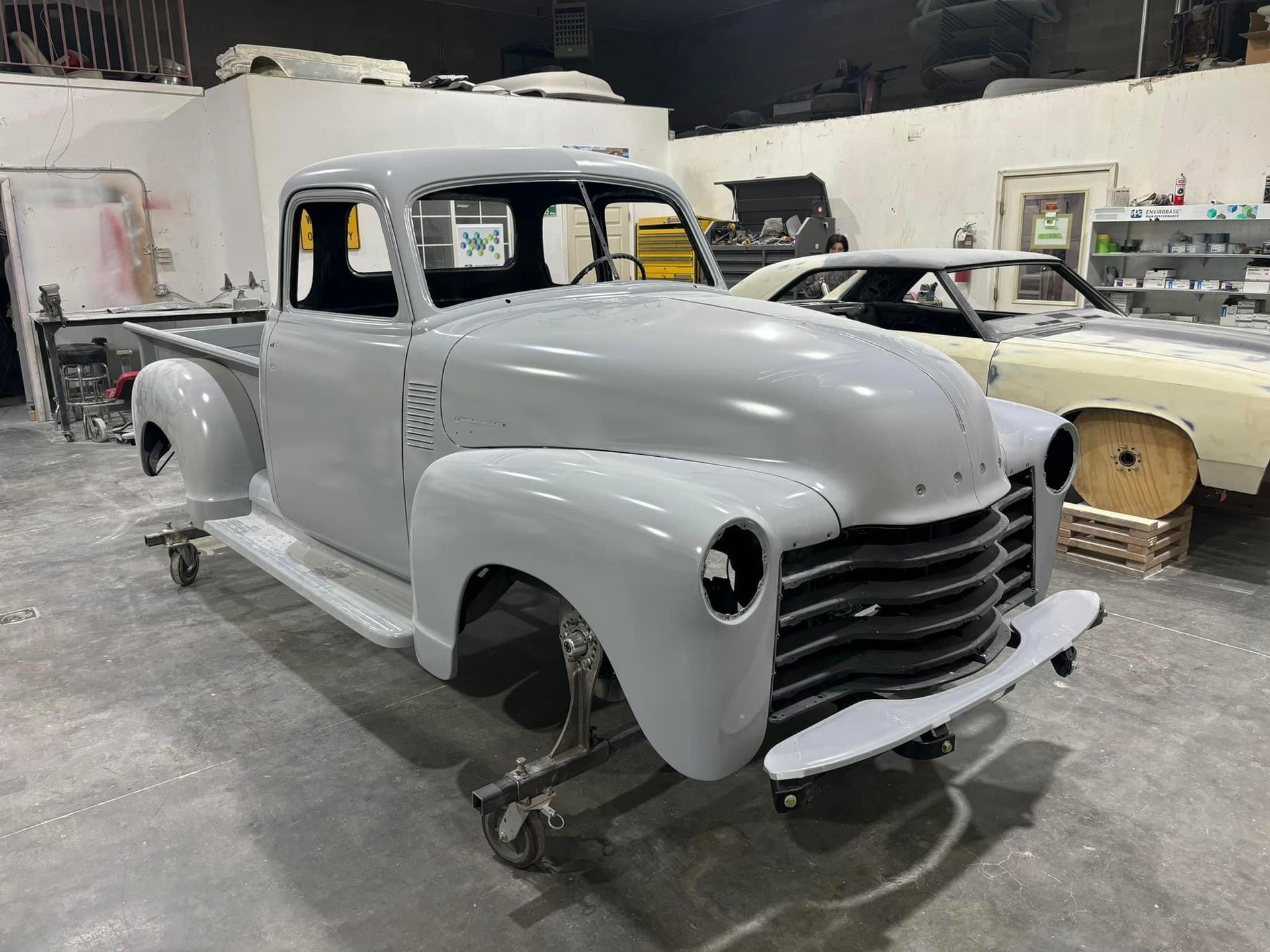 An old pickup truck is sitting on a dolly in a garage.