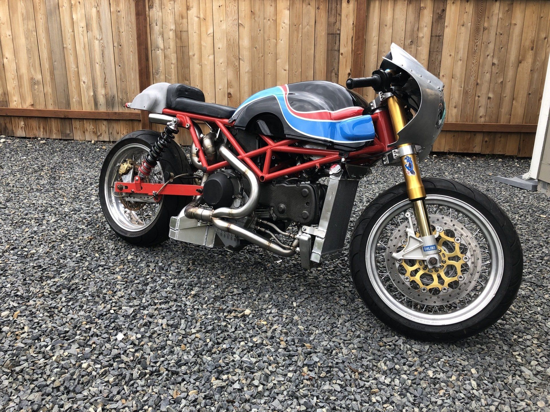 A motorcycle is parked on gravel in front of a wooden fence.