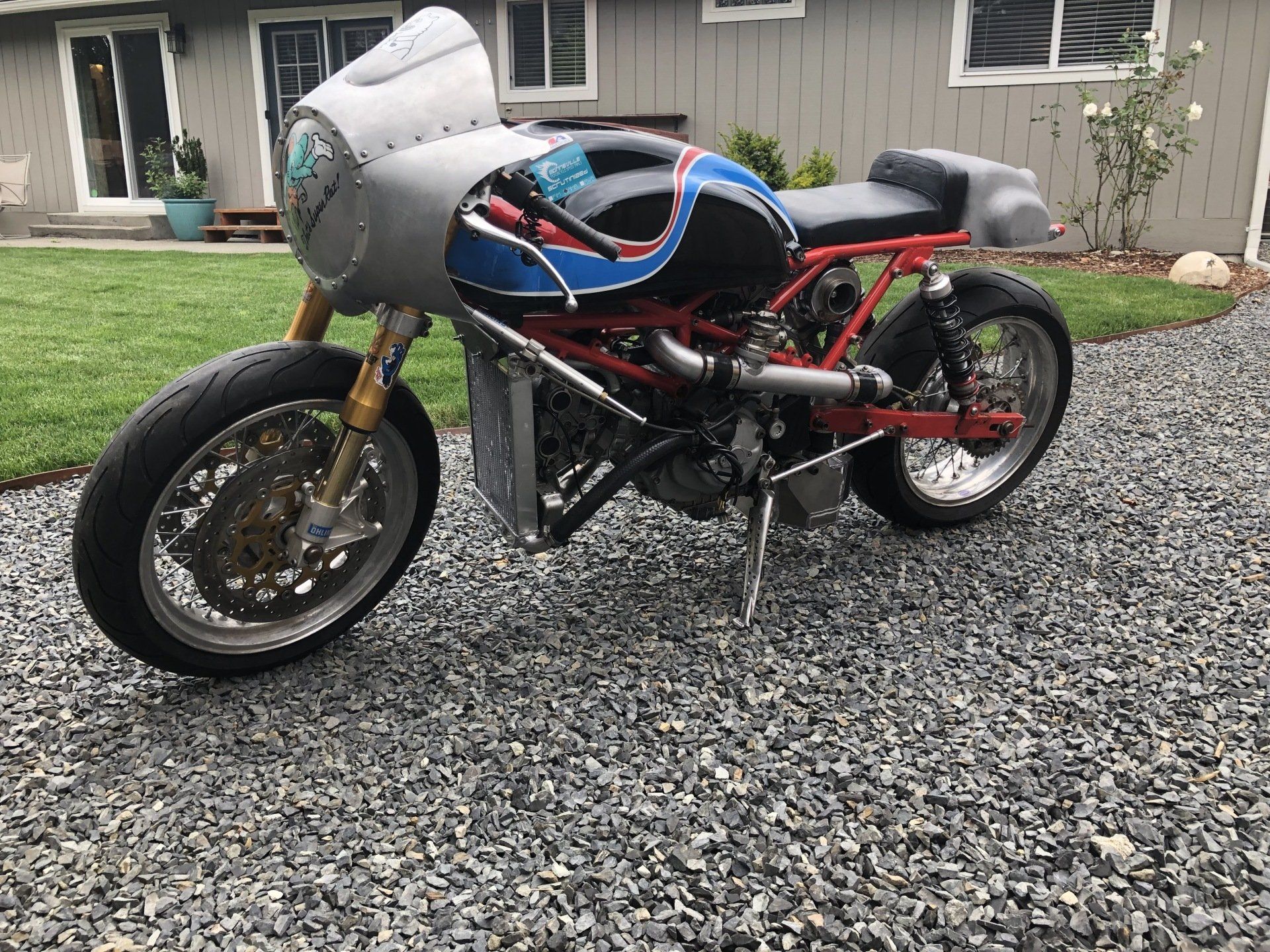A motorcycle is parked on gravel in front of a house.
