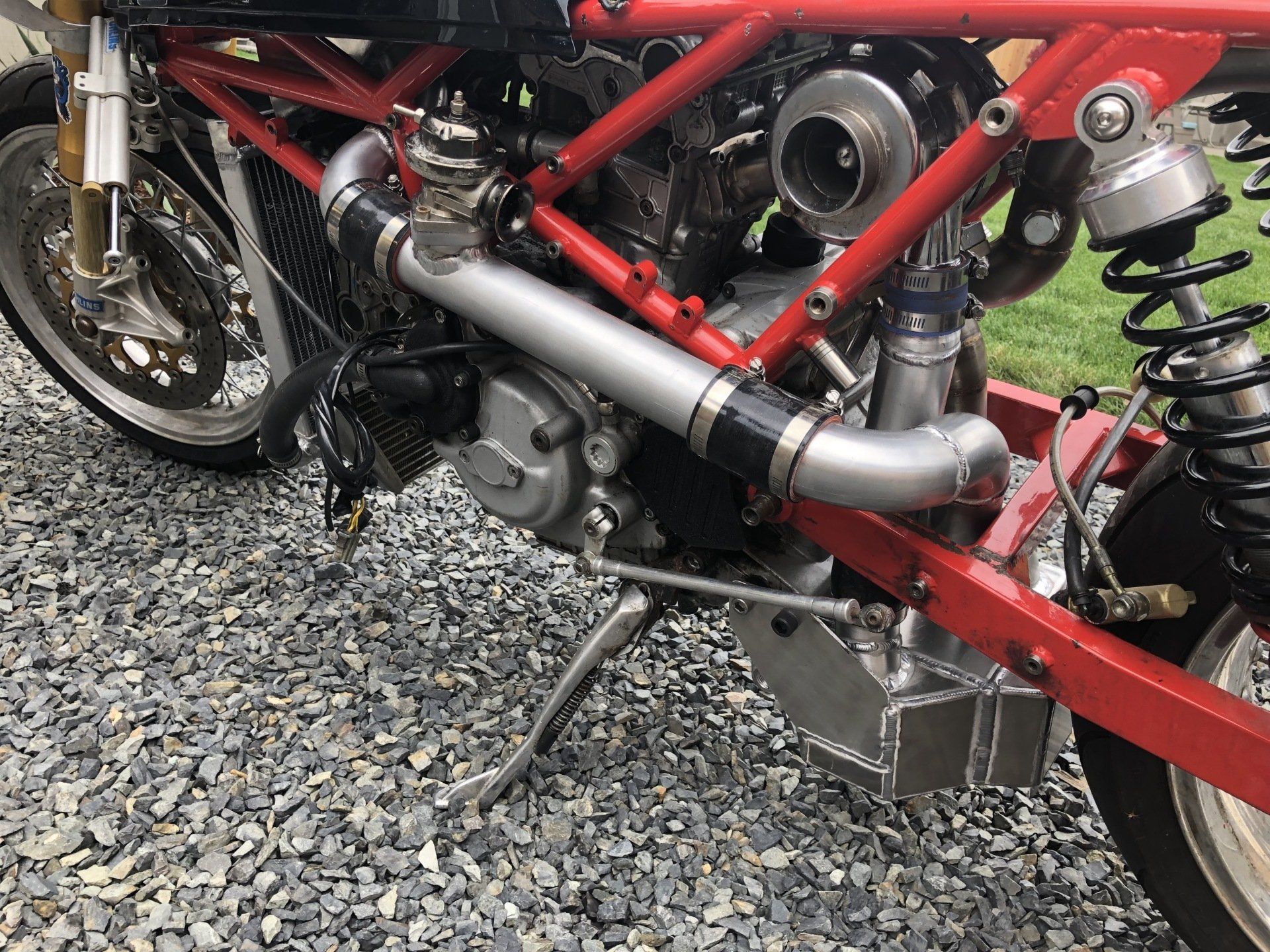 A red motorcycle with a turbocharger on the engine is parked on gravel.