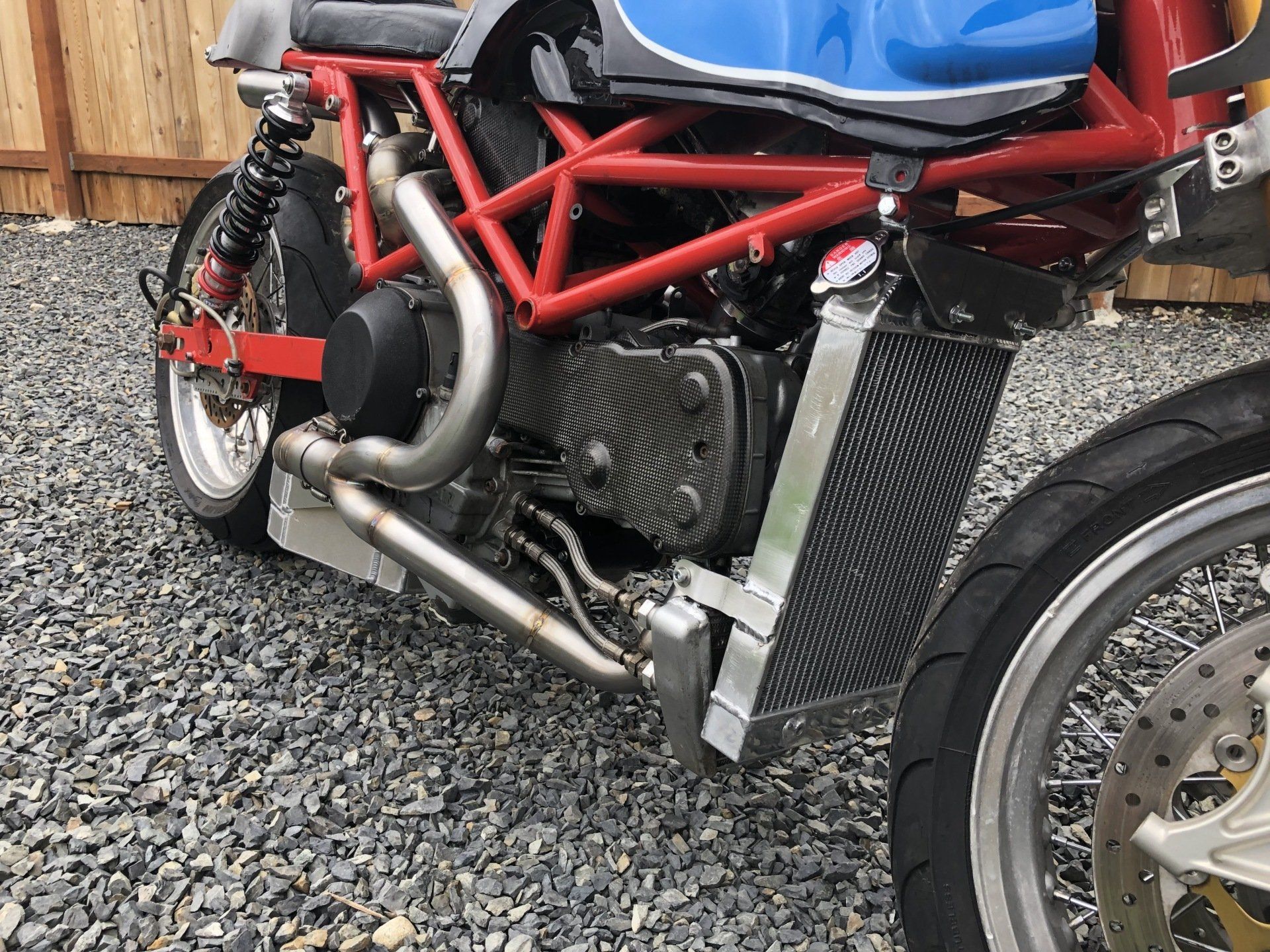 A red and blue motorcycle is parked on gravel next to a fence.