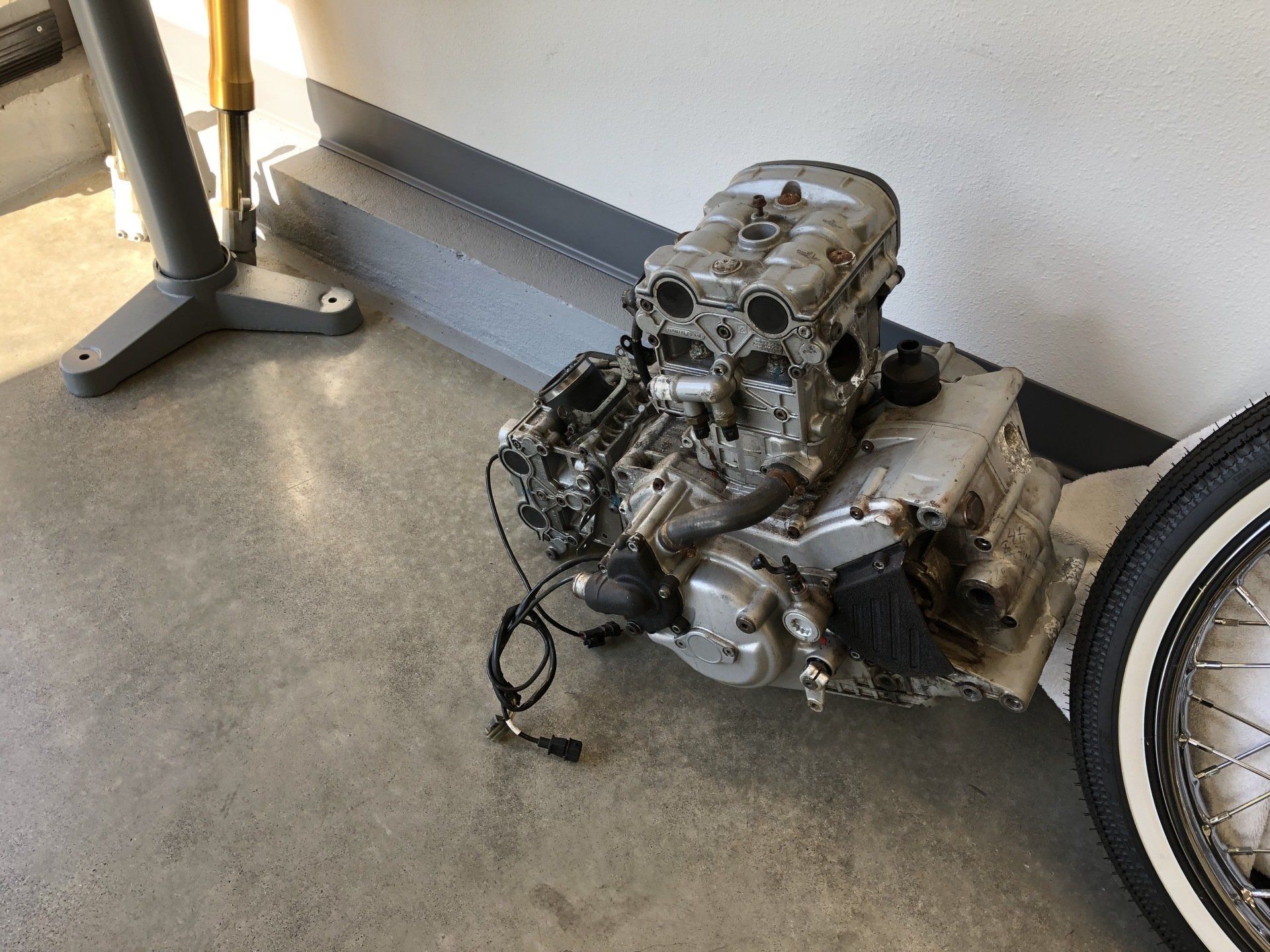 A motorcycle engine is sitting on the floor next to a tire.