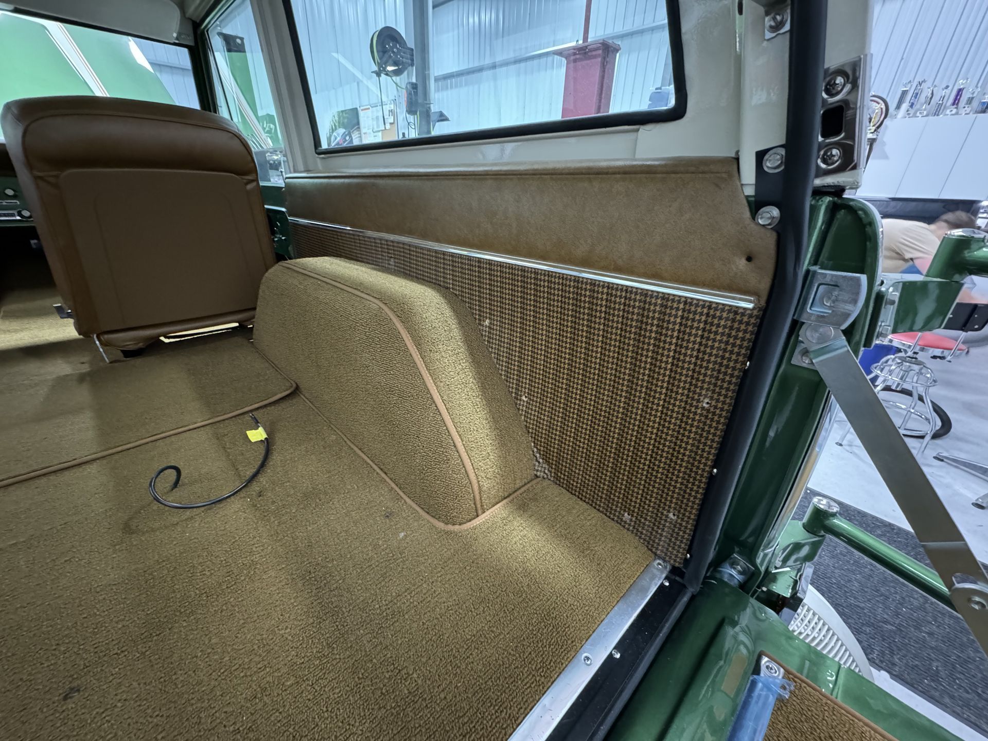 The back seat of a green jeep with a brown seat and carpet.