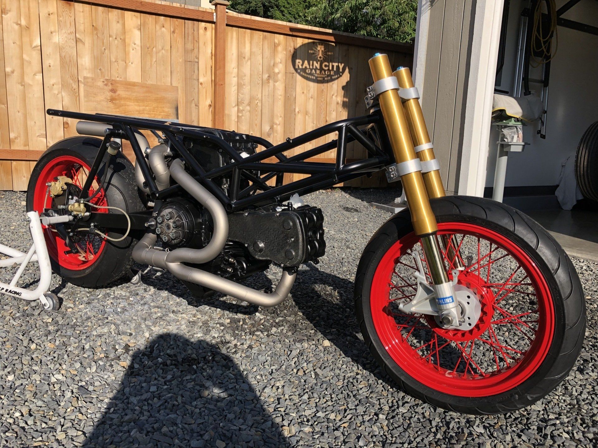 A motorcycle with red wheels is parked in front of a garage.