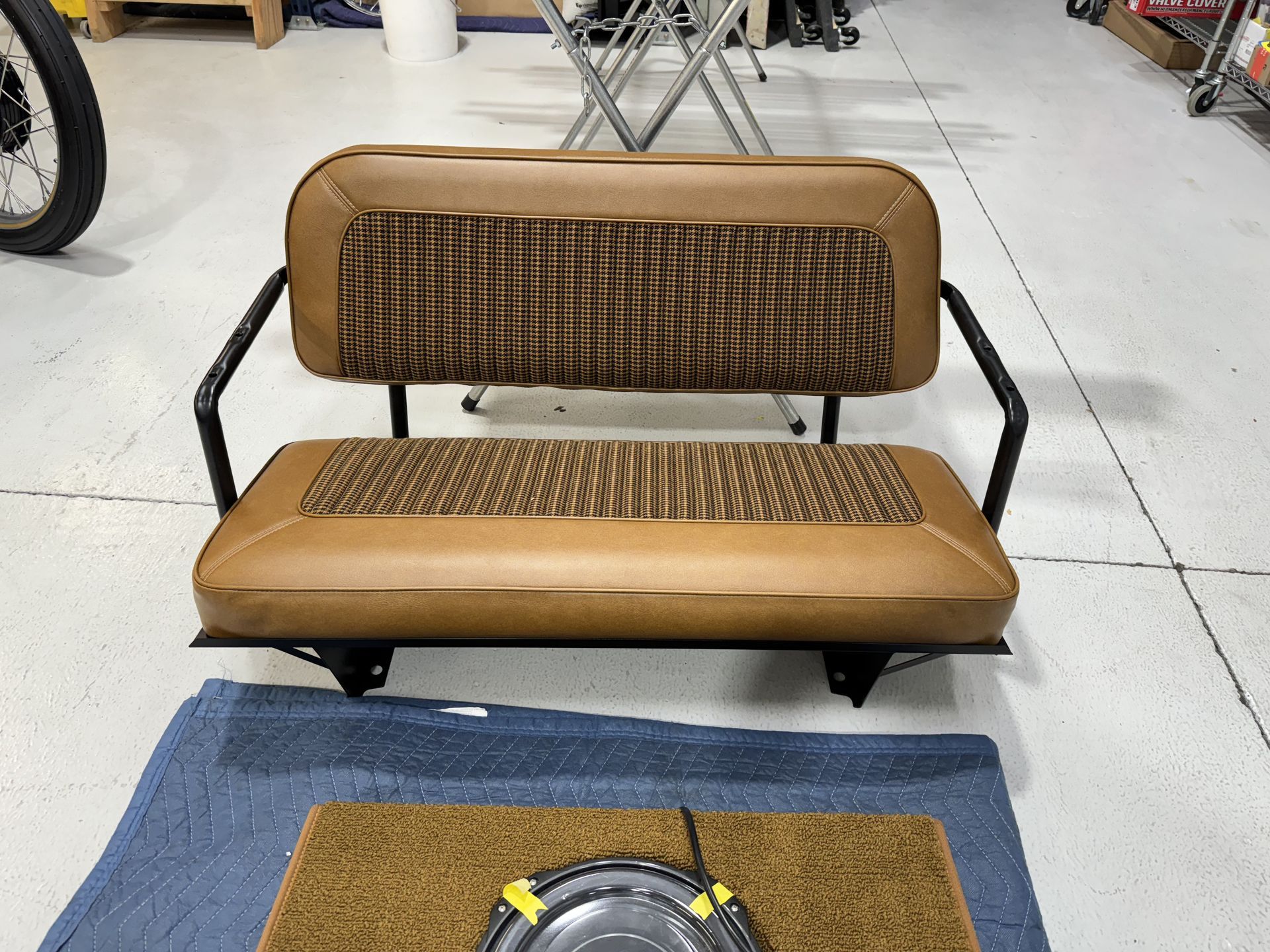 A brown bench is sitting in a garage next to a door mat.